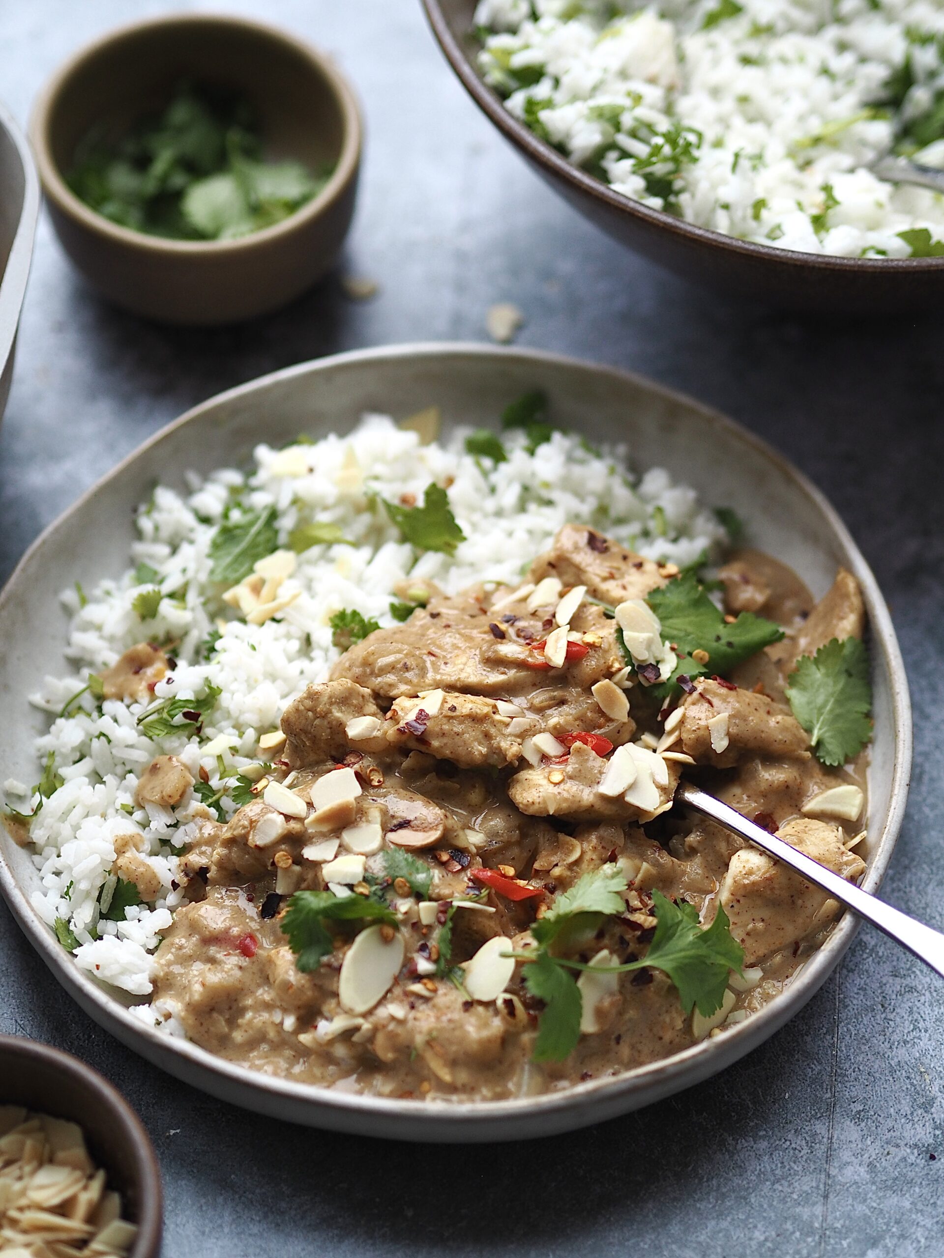 Grey bowl of white rice with coriander and chicken curry topped with toasted almonds.