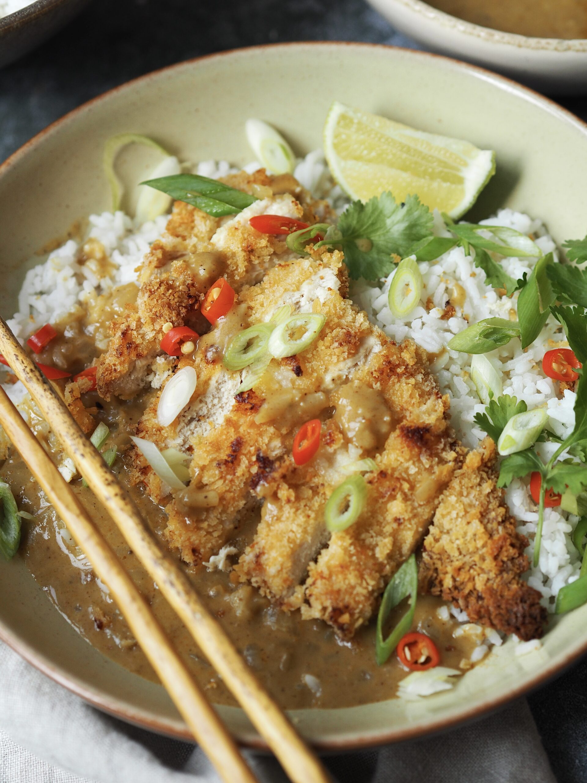 Close up of a chicken katsu curry rice bowl with a pair of wooden chopsticks on the side.