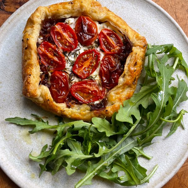 Cherry tomato, goats cheese and red onion galette on a white plate with a tangle of rocket.