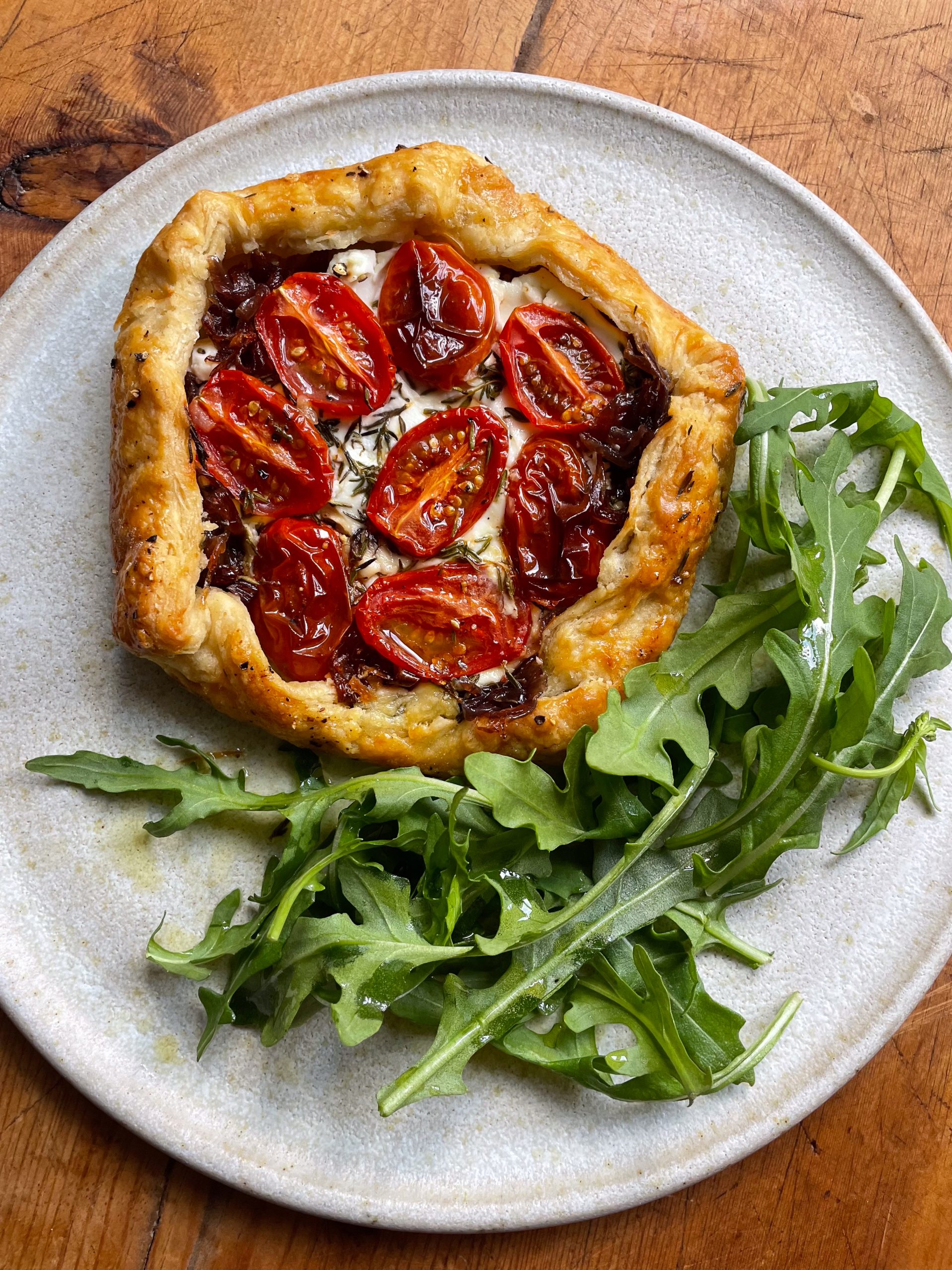 Cherry tomato, goats cheese and red onion galette on a white plate with a tangle of rocket.