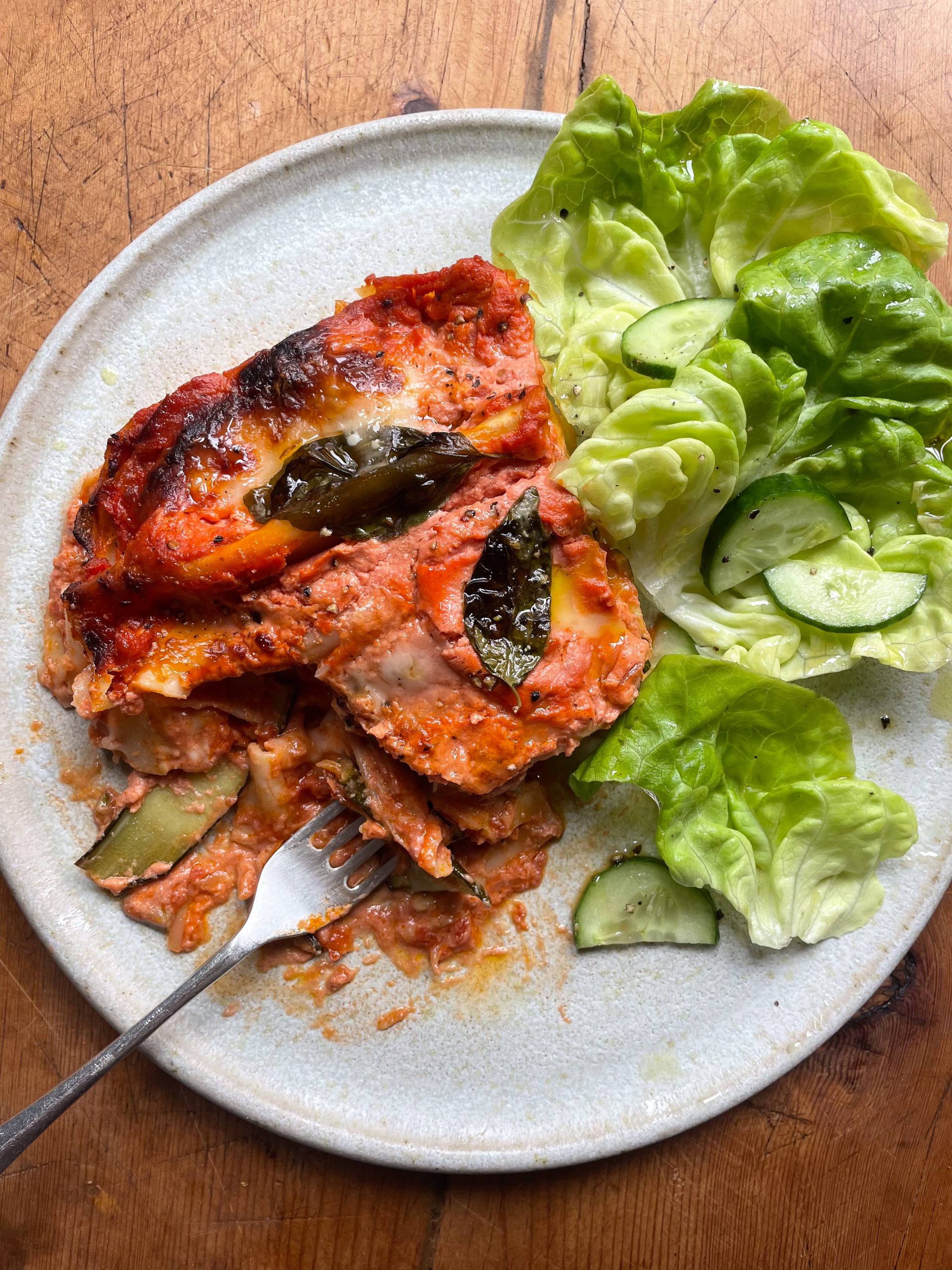 Piece of courgette lasagna on a white plate with a lettuce and cucumber salad.