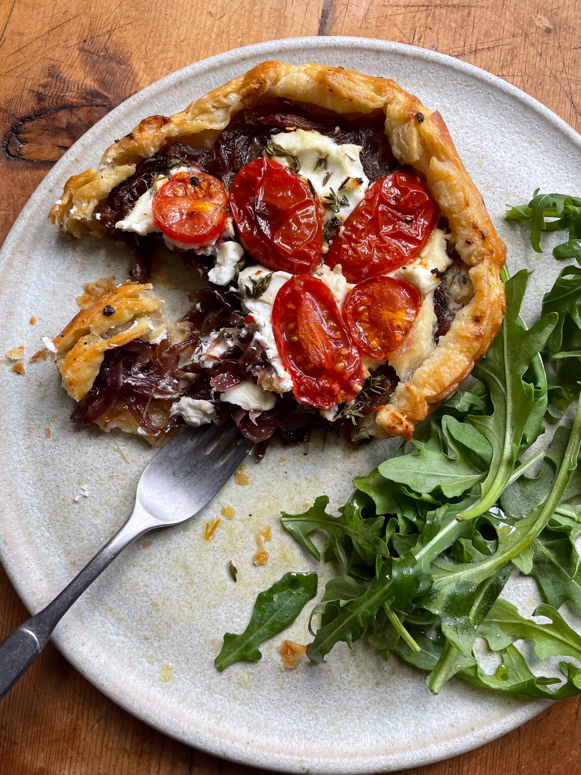 A fork cutting into a caramelised onion, cherry tomato and goats cheese galette. 