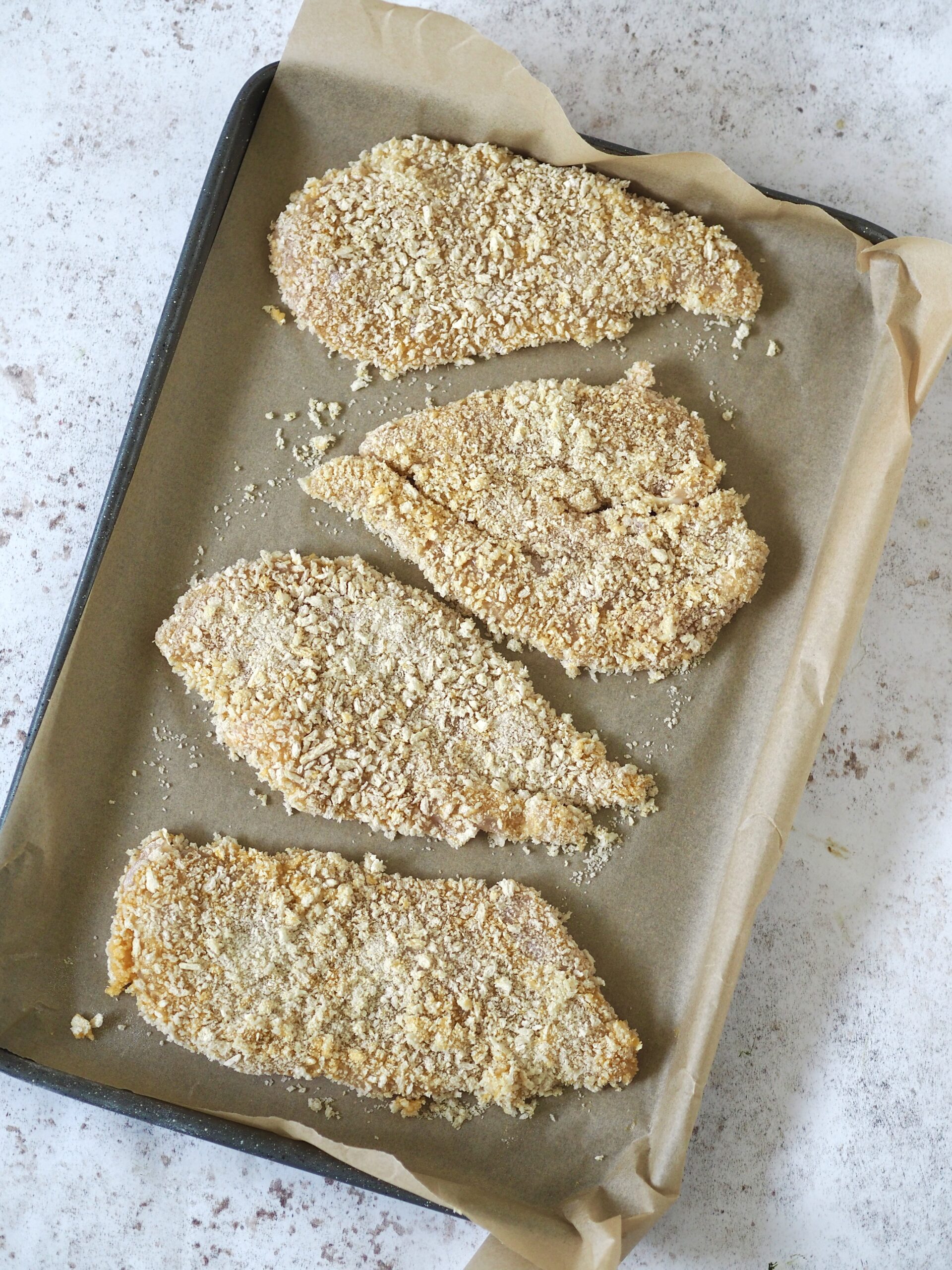 Panko breadcrumb coated chicken cutlets on a lined baking tray.