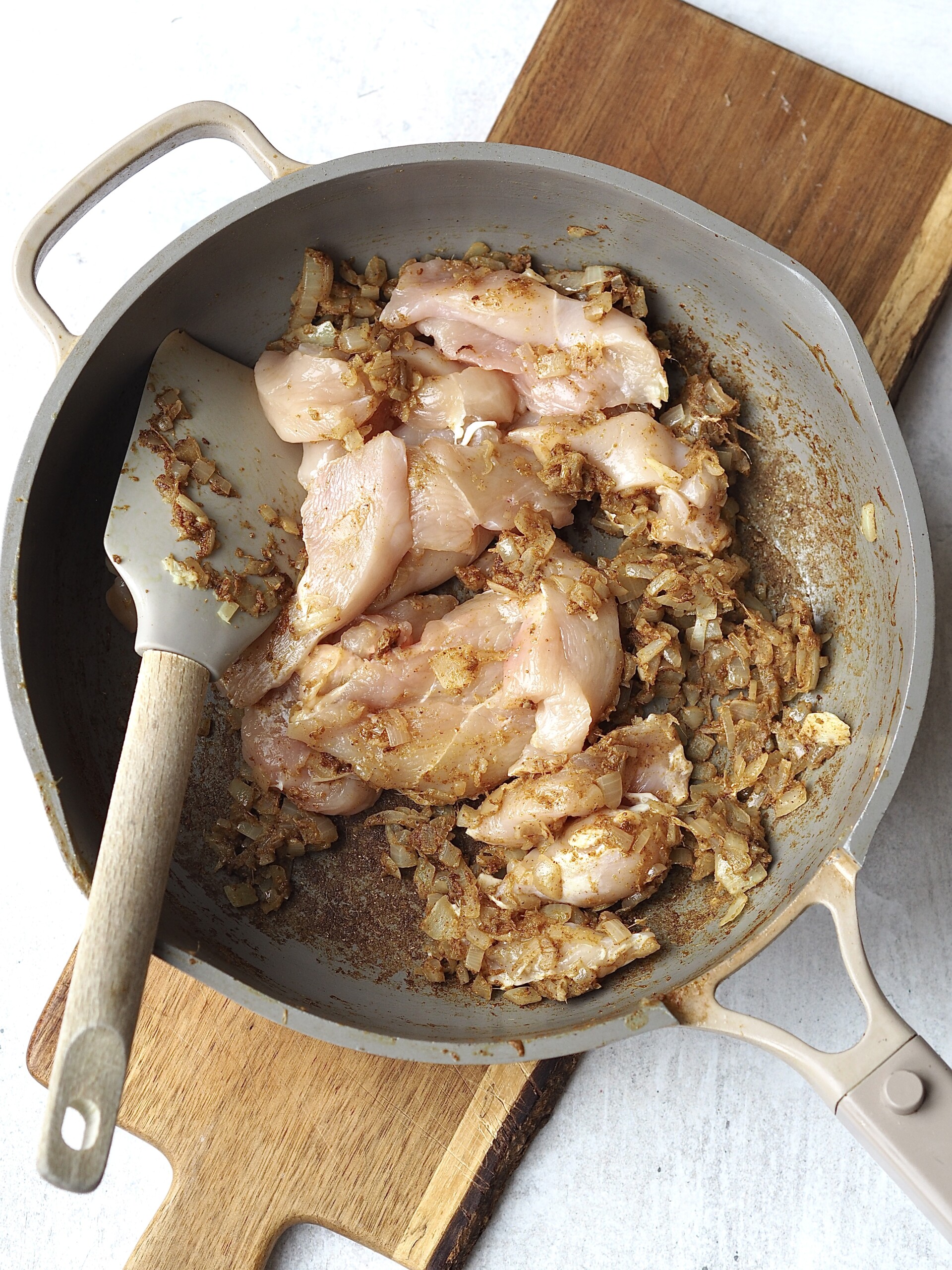 Sliced chicken breast bring stirred into a frying pan of cooked onions and raw spices.