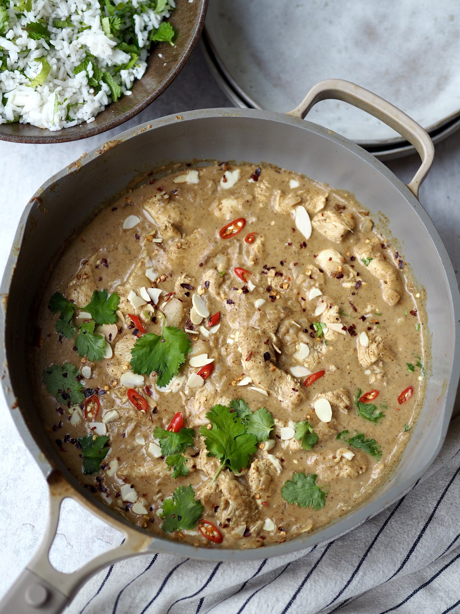 Almond butter chicken curry topped with fresh coriander and red chilli in a grey frying pan.