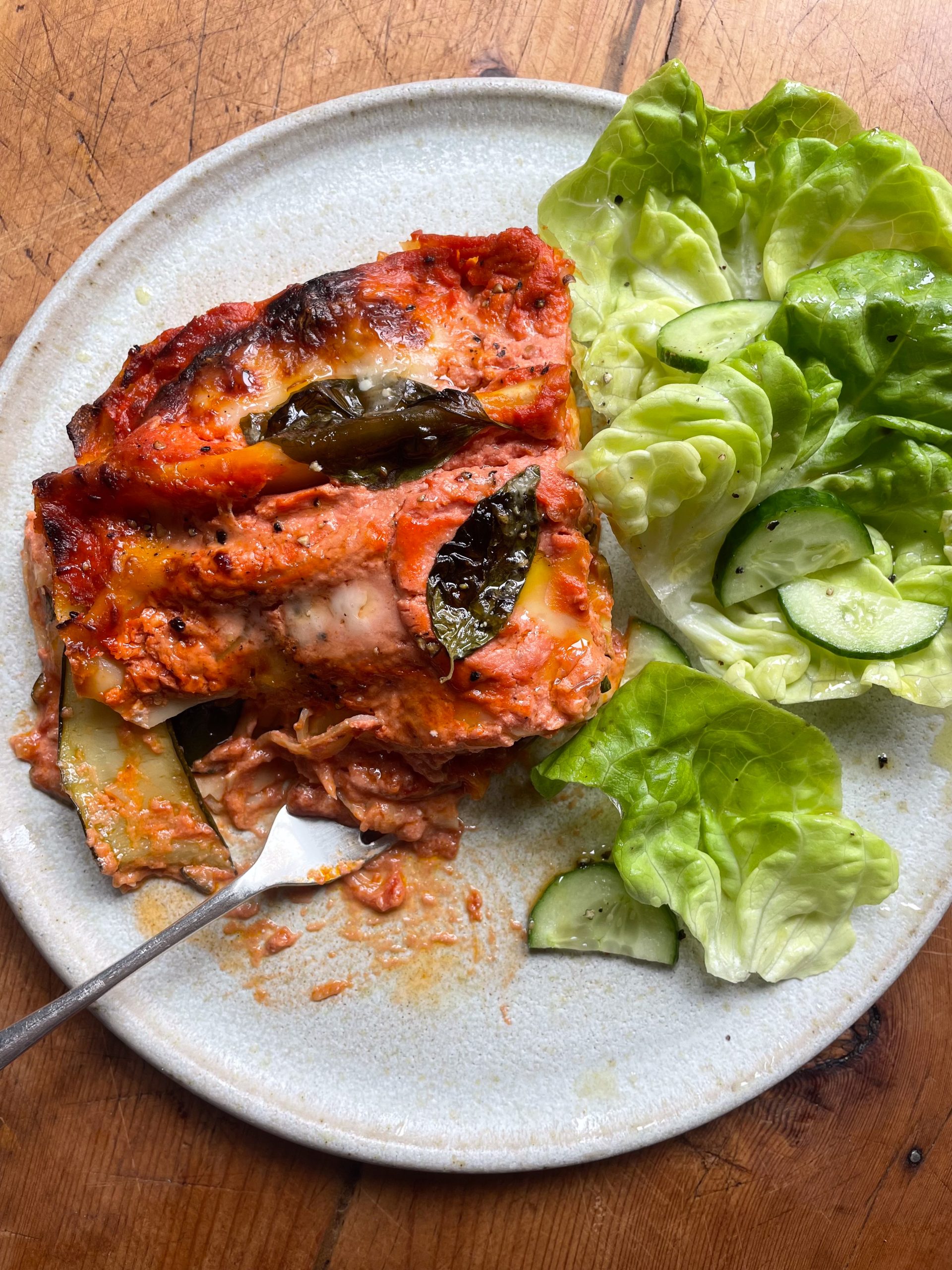 Courgette lasagna on a white plate with a green side salad.