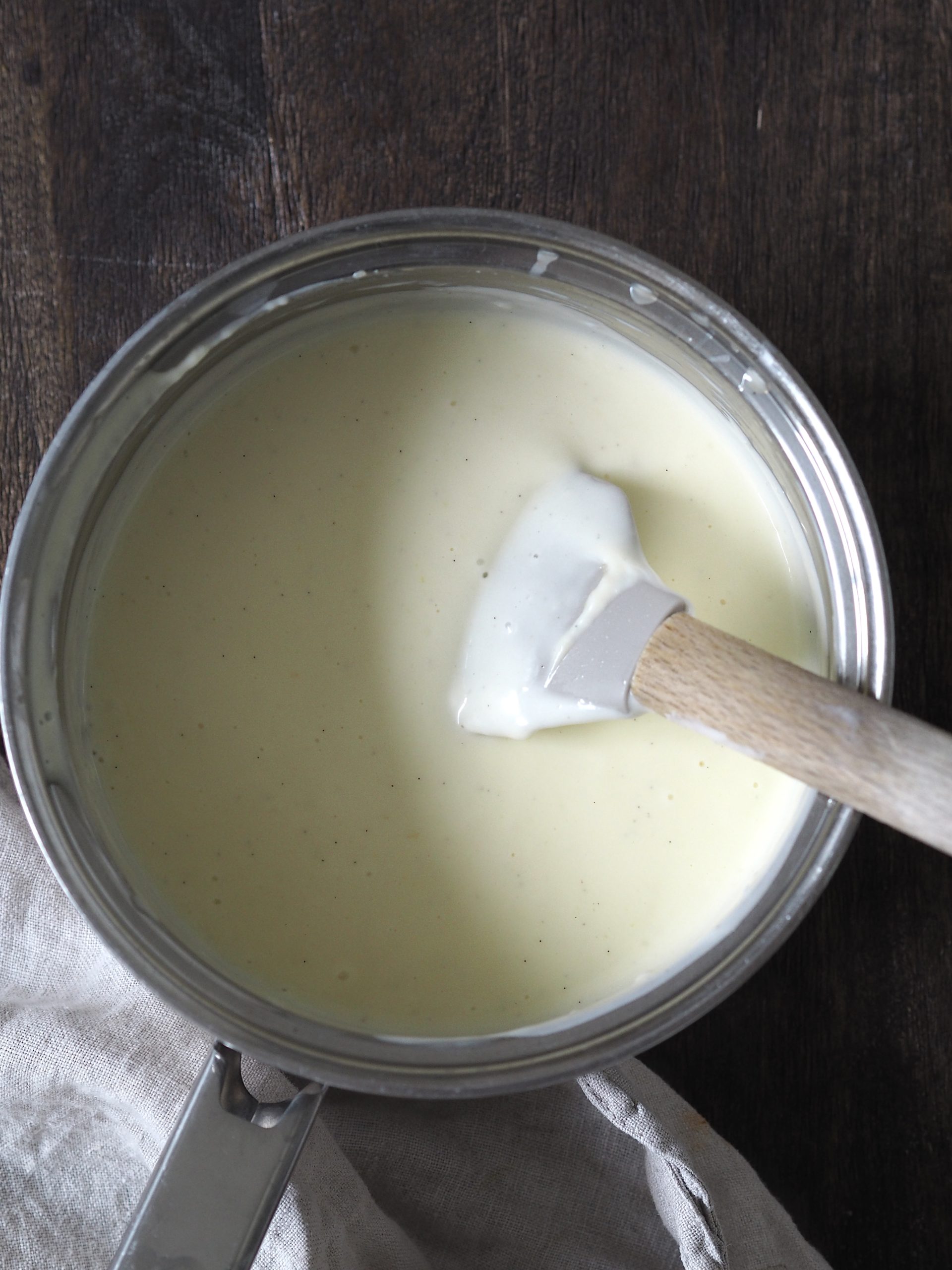 A rubber spatula stirring a saucepan of custard.