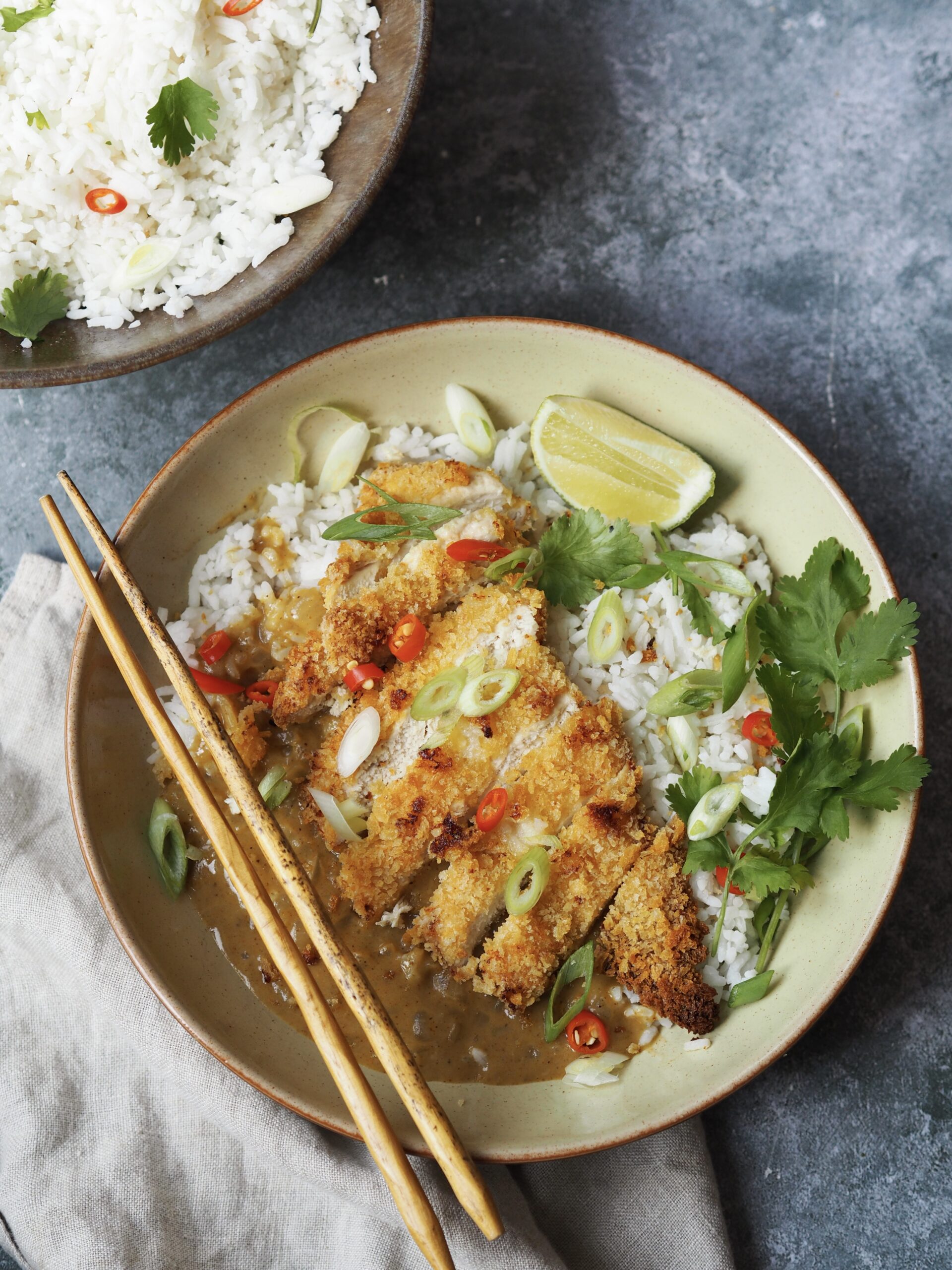 Overhead vew of a chicken katsu and curry sauce rice bowl on a grey stone background.