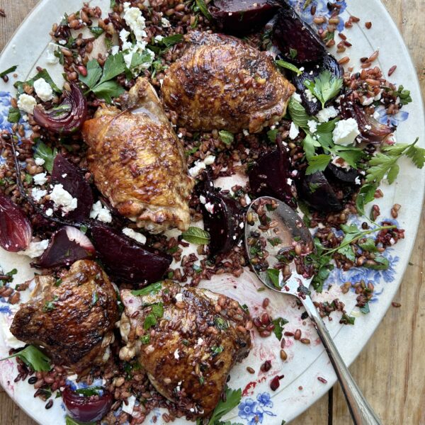 Blue and white serving platter of roasted chicken thighs, beetroot and red onion over mixed grains.