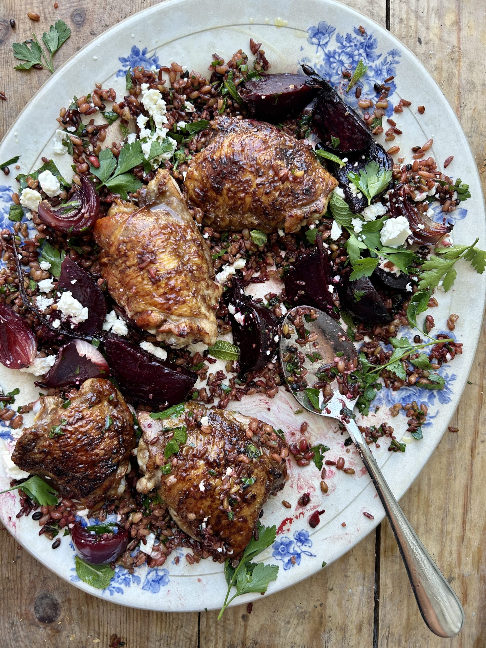 Blue and white serving platter of roasted chicken thighs, beetroot and red onion over mixed grains. 