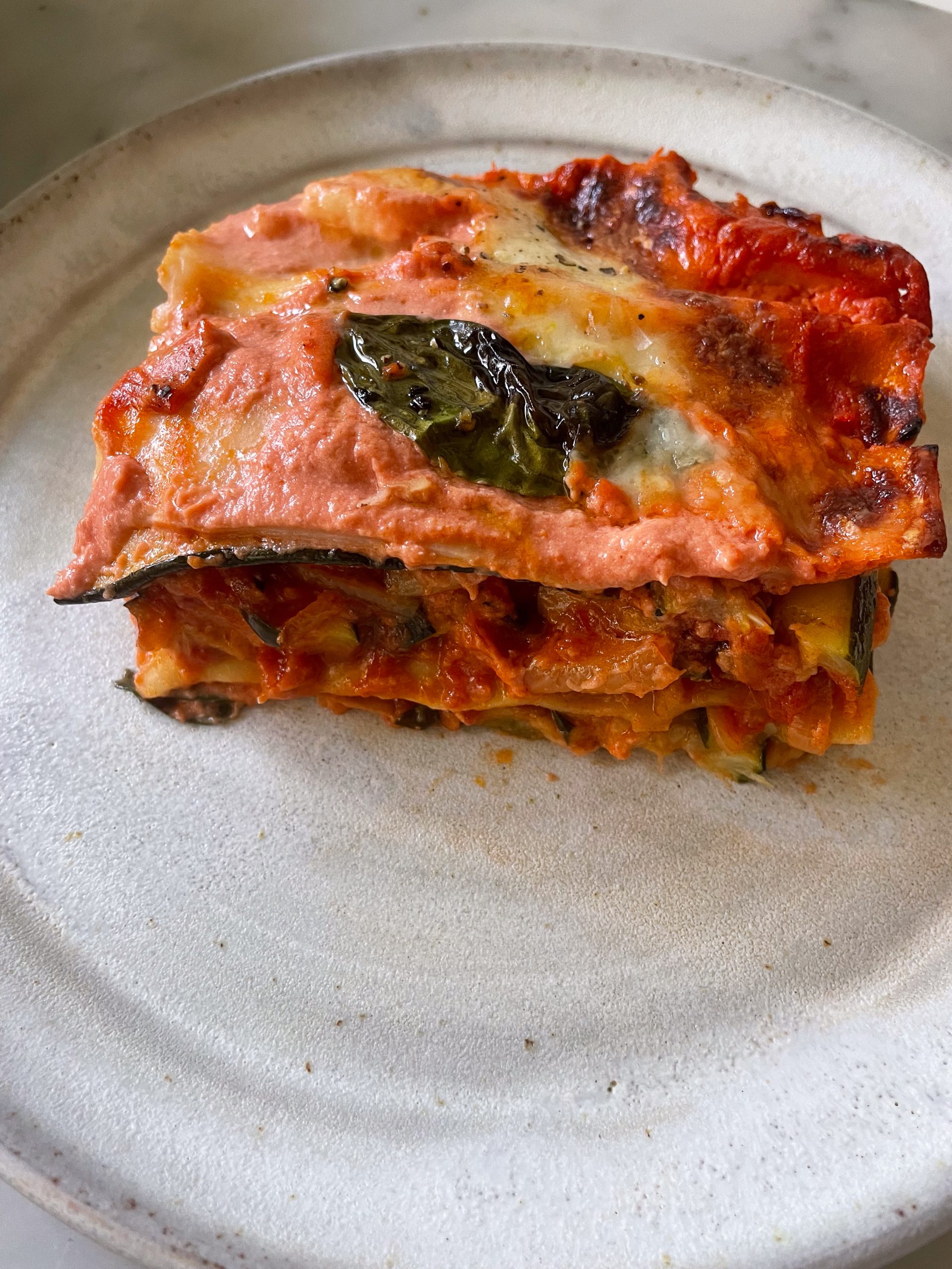 Side on view of a piece of zucchini lasagna on a white plate.