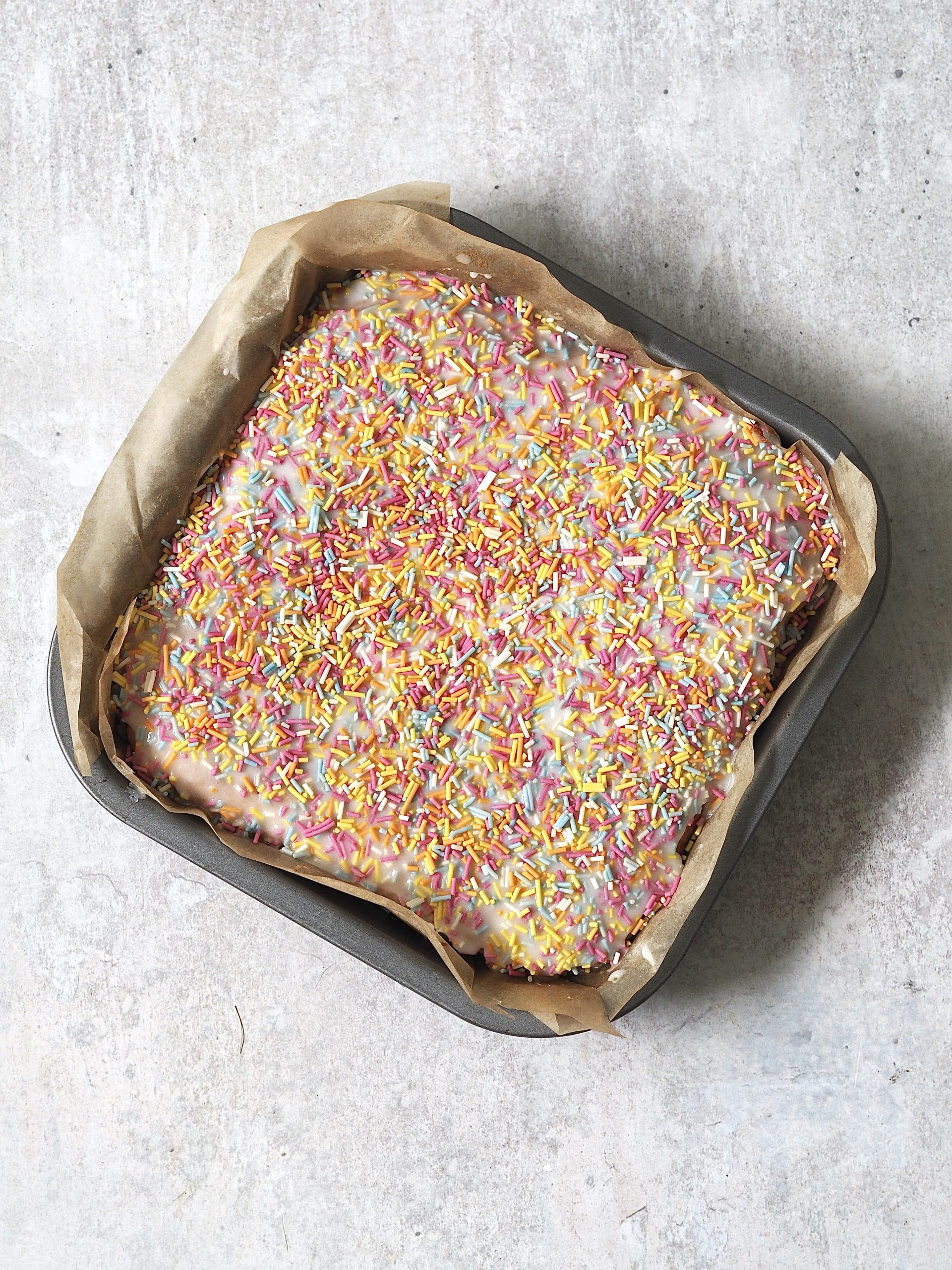 Iced and sprinkle decorated school sponge in a lined tin.