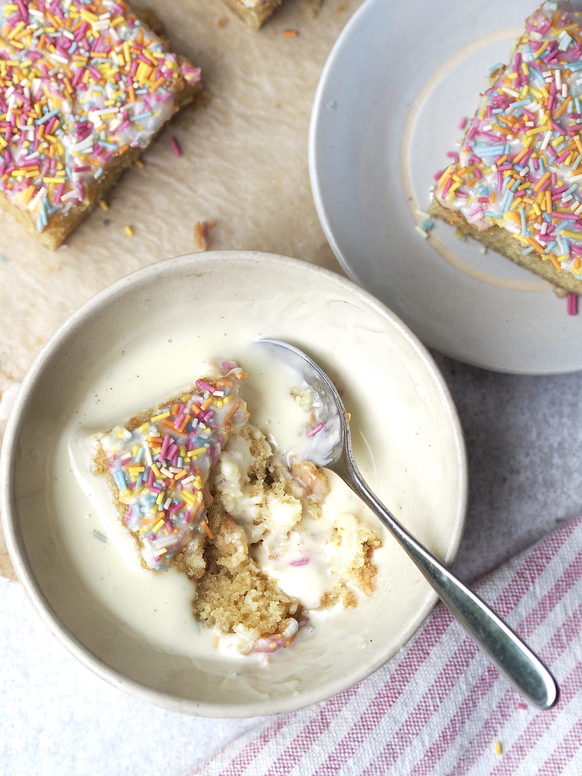 Bowl of school dinner sponge and rainbow sprinkles with custard.