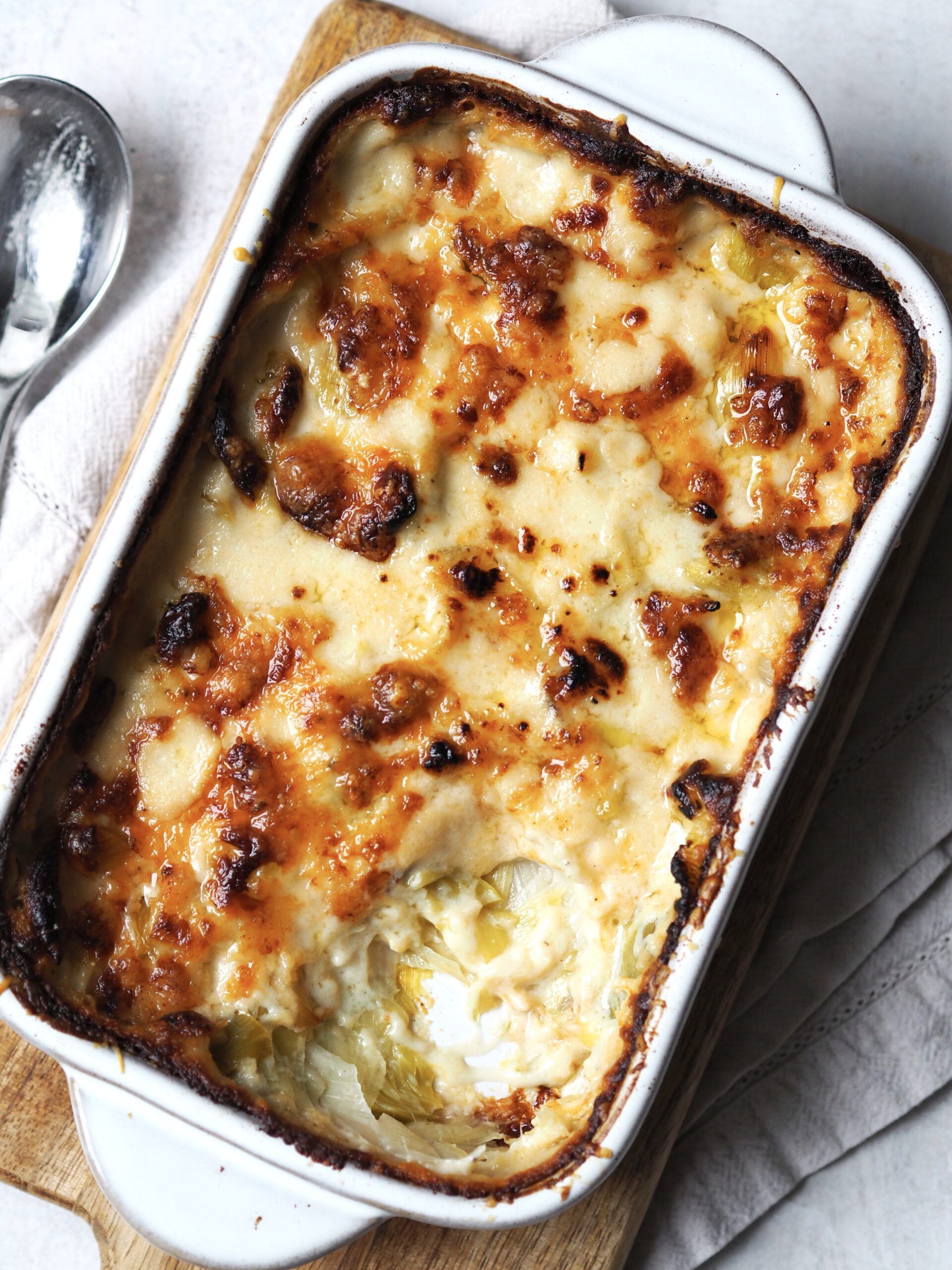 Close up of a white pan of cheesy leeks with a golden cheese top.