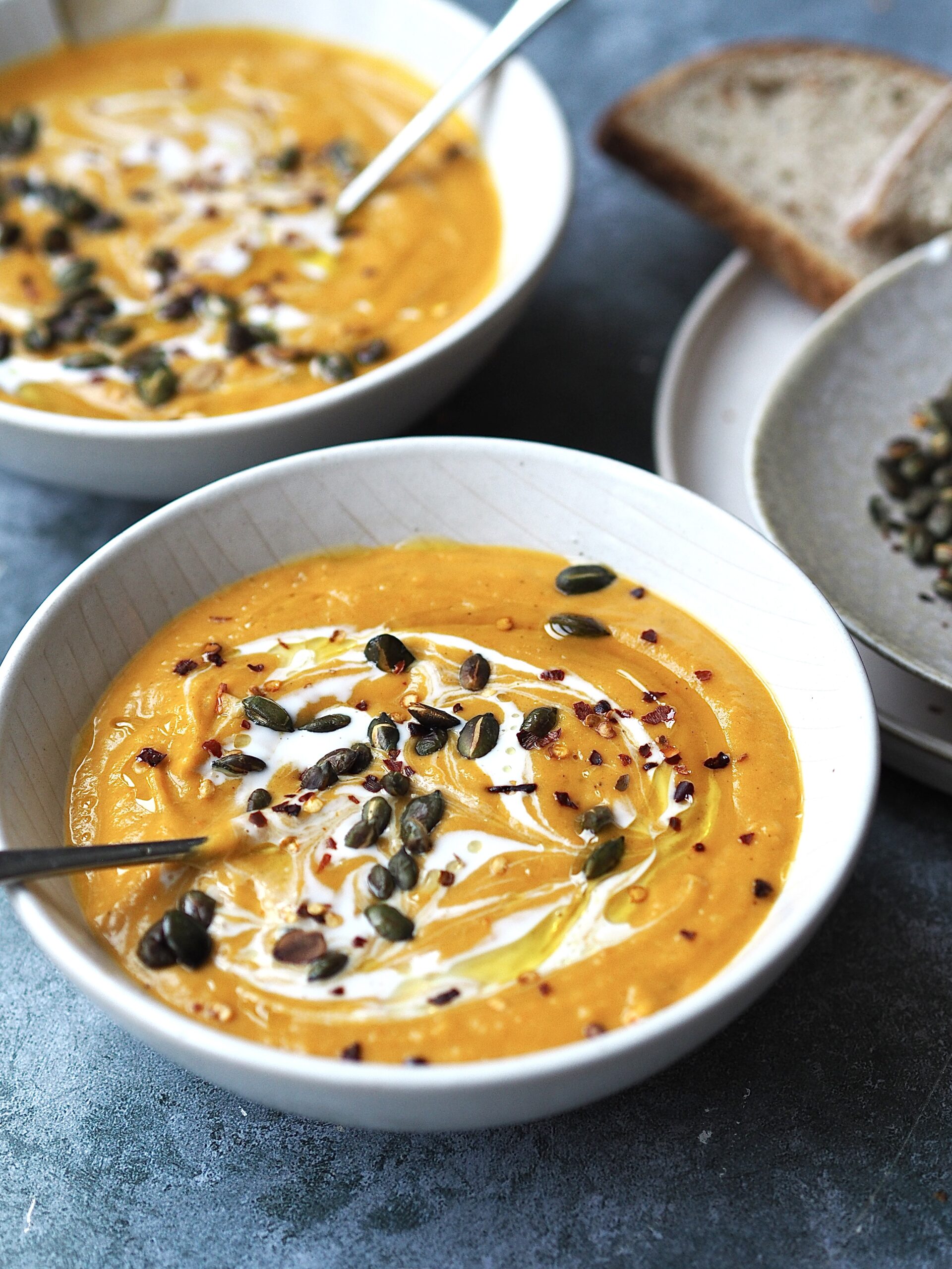 White bowls of roasted butternut squash soup topped with toasted pumpkin seeds. 