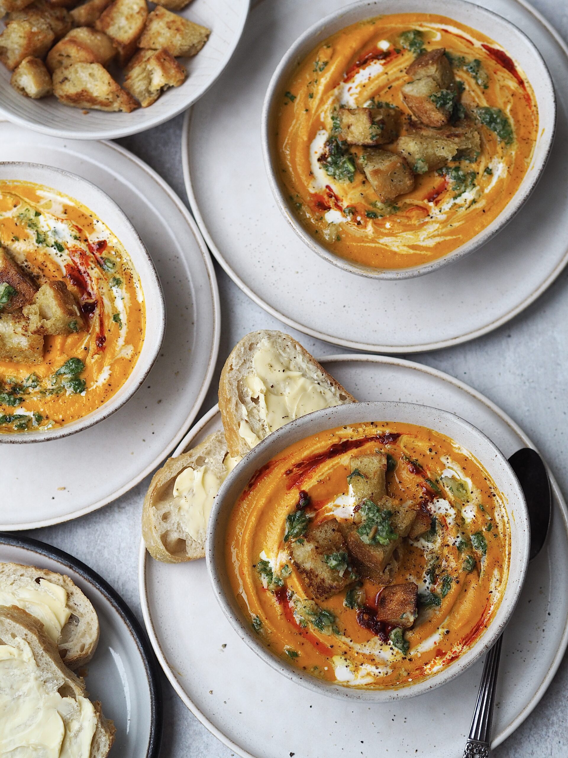 Grey bowls of carrot soup topped with homemade pesto and croutons.