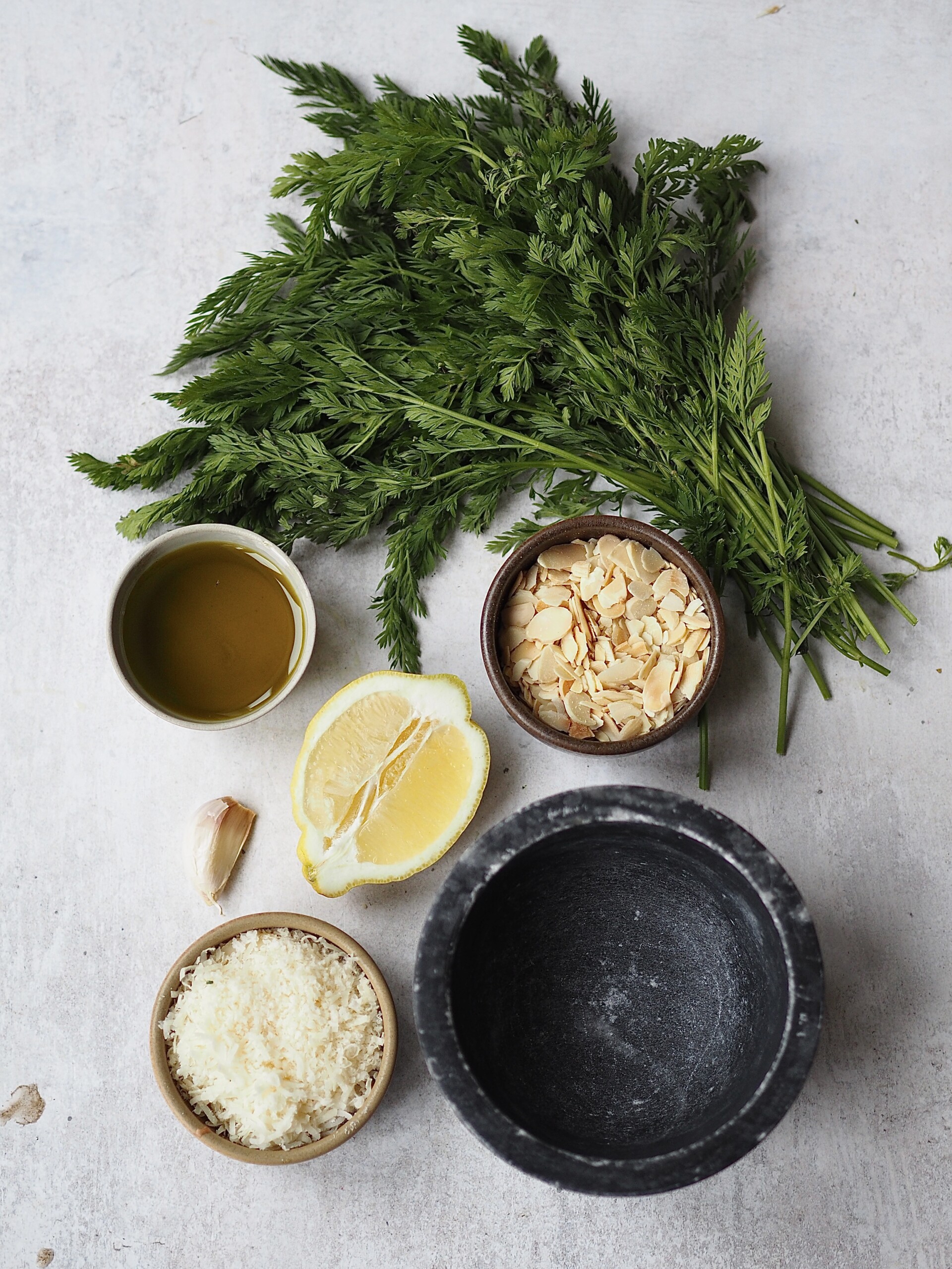 Ingredients to make carrot top pesto on a grey countertop. 