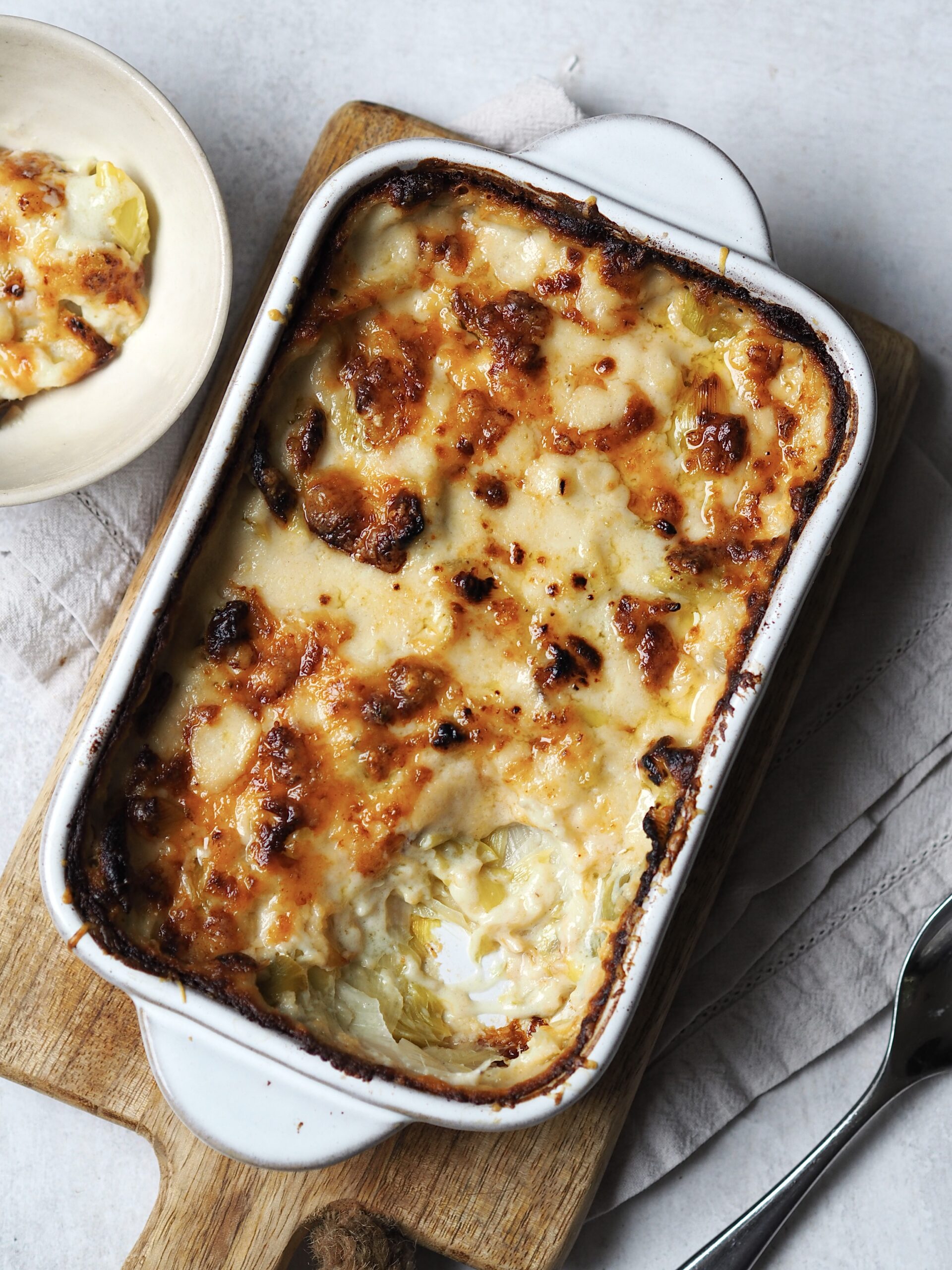 Overhead picture of cheesy baked leeks with a spoonful taken out and placed on a side plate.