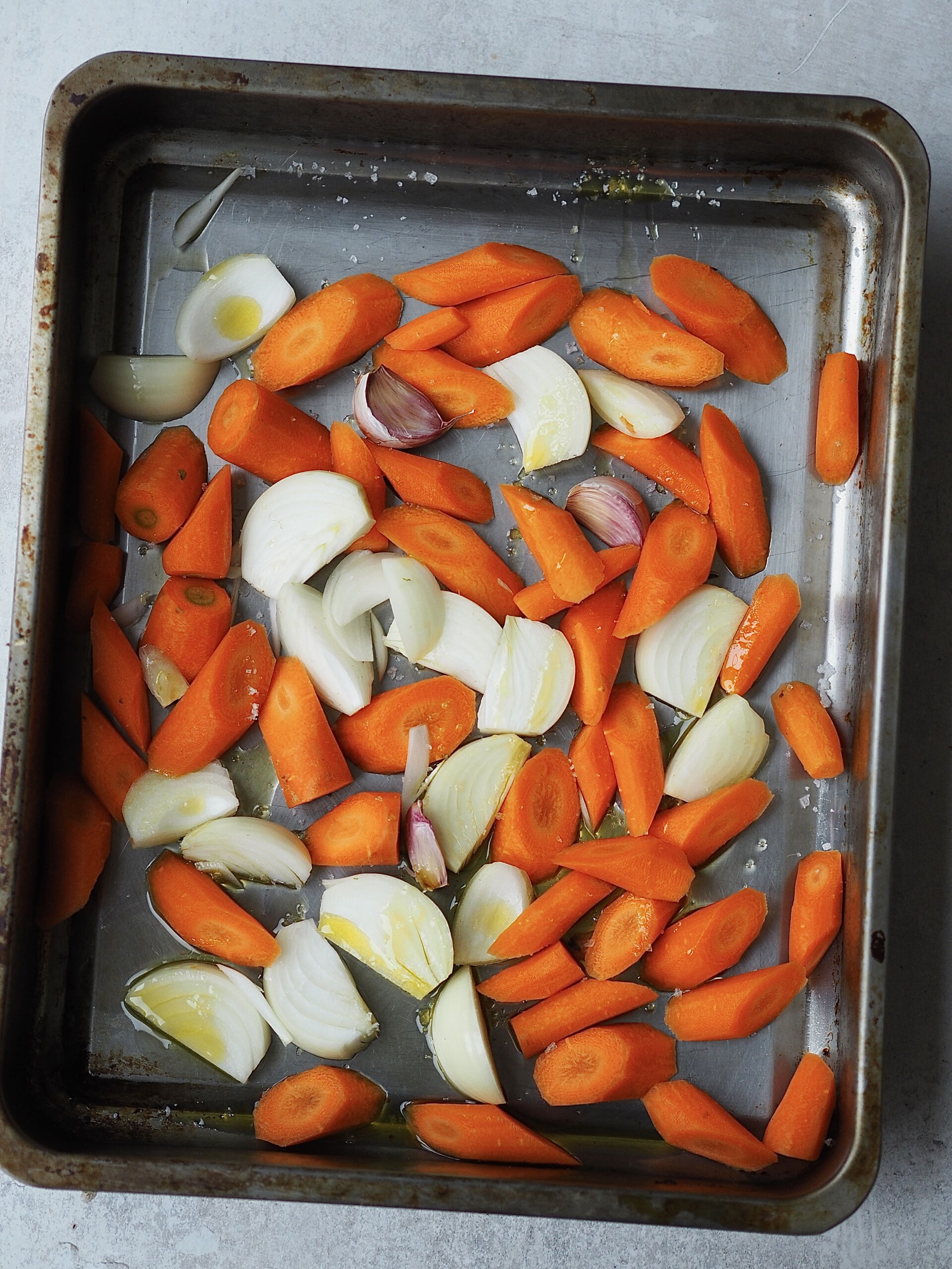 Roasting tray of chopped carrots, onions and garlic.