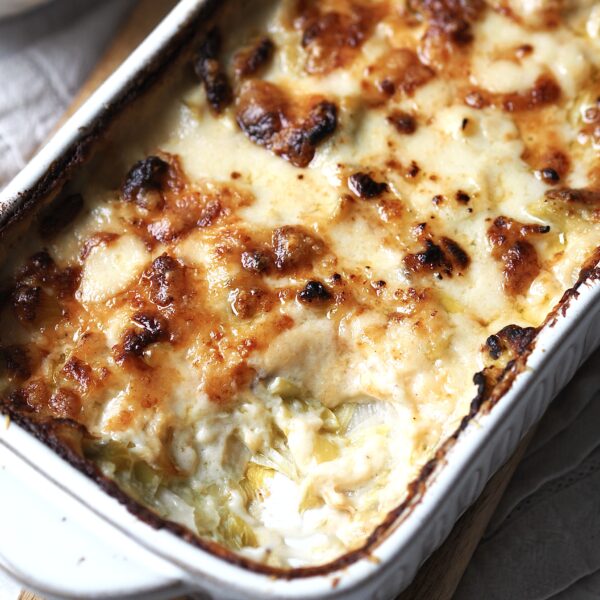 Close up of a white baking dish of cheesy leeks with a spoonful taken out.