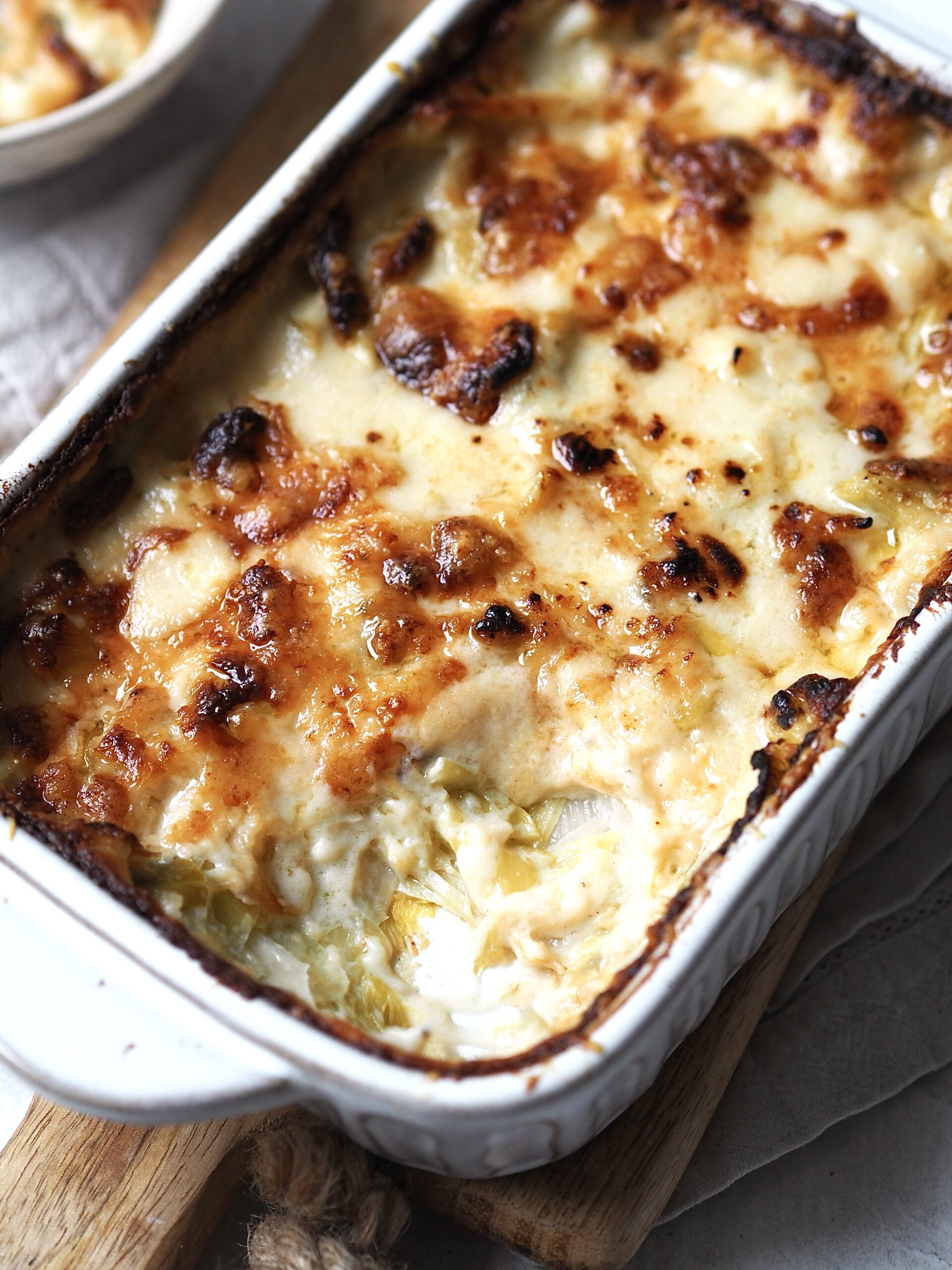 Close up of a white baking dish of cheesy leeks with a spoonful taken out. 