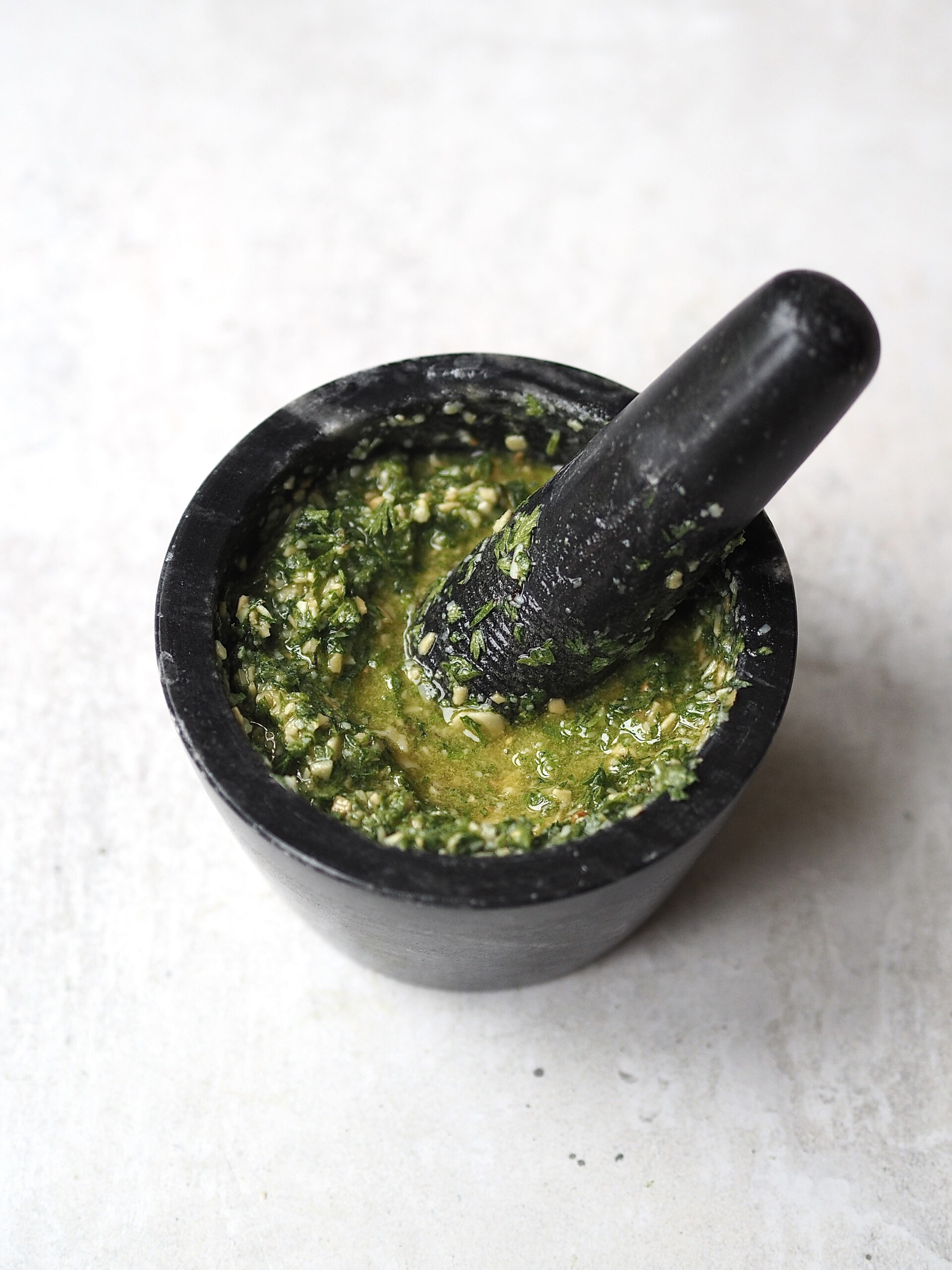 Carrot top pesto being made in a dark grey mortar and pestle. 