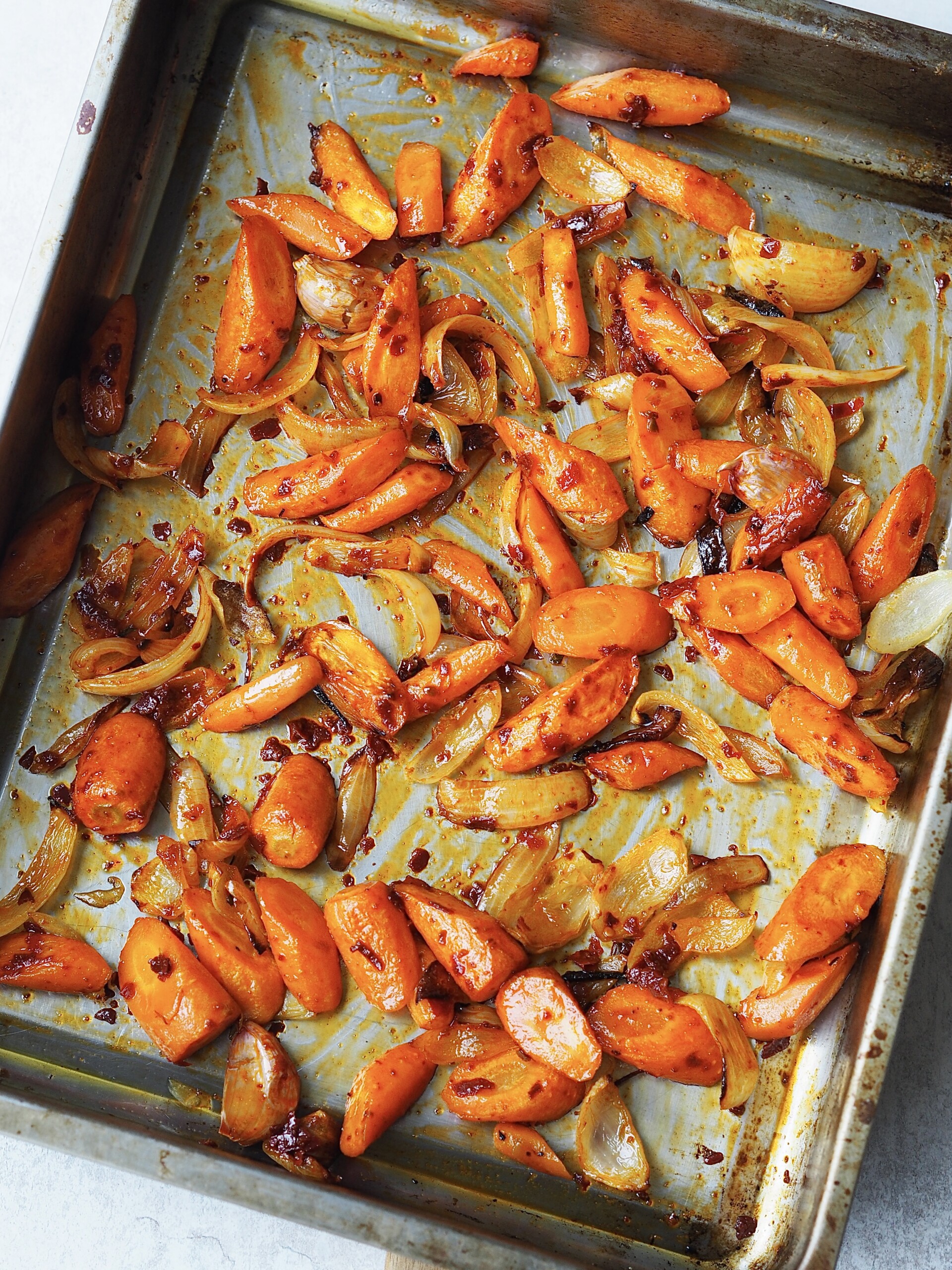 Roasted vegetables tossed with harissa on a roasting tray.