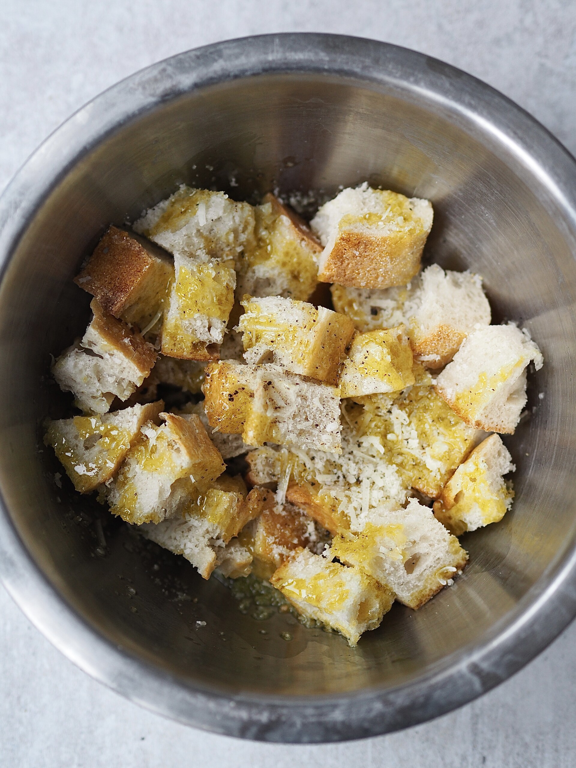 Bread cubes tossed with grated cheese, olive oil and seasonings in a metal bowl.