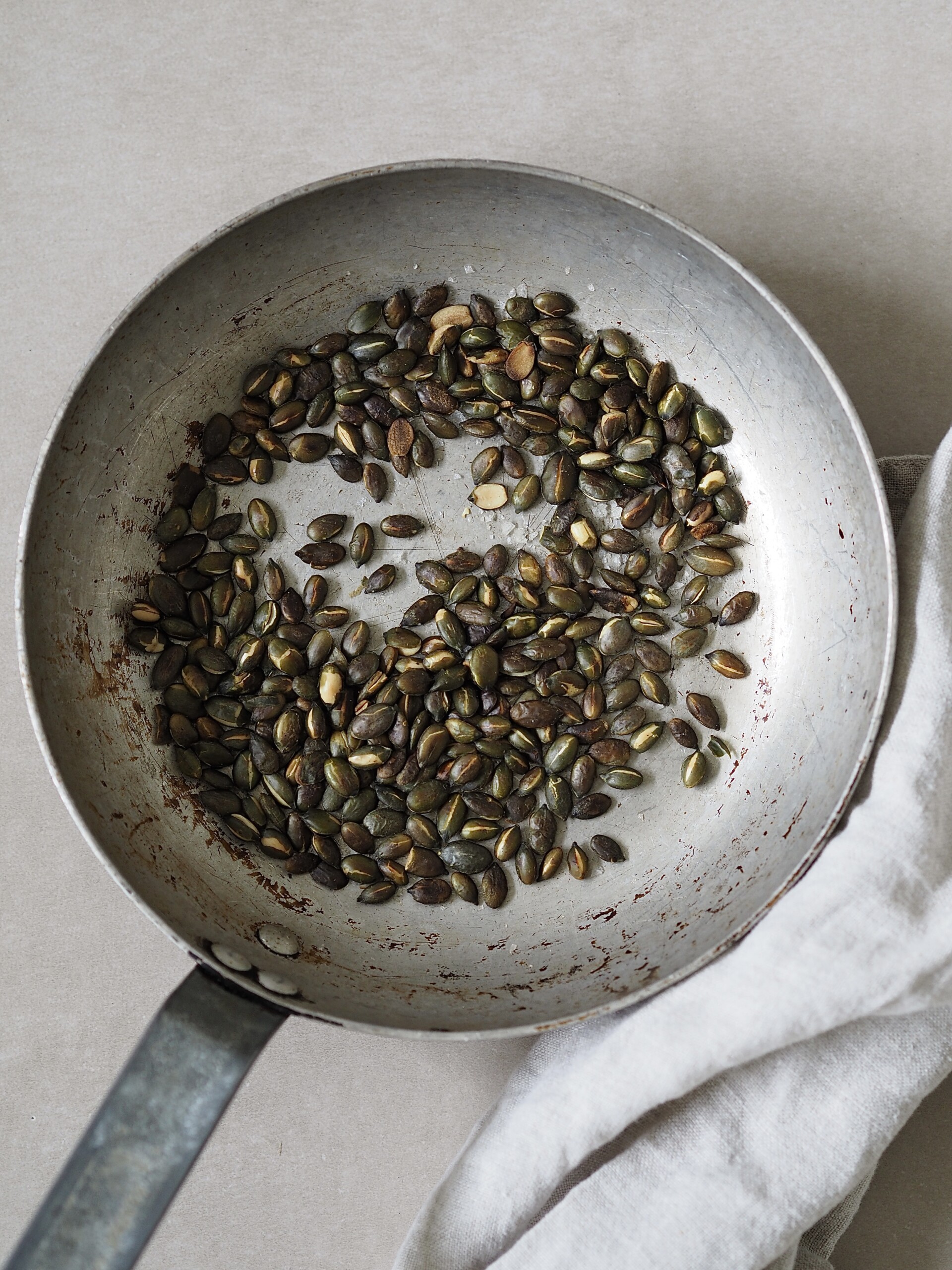 Toasted pumpkin seeds in a grey frying pan.