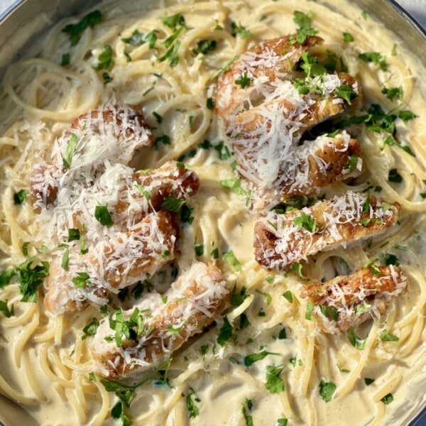 creamy chicken pasta in a pan with a fork, with chicken sliced on top..