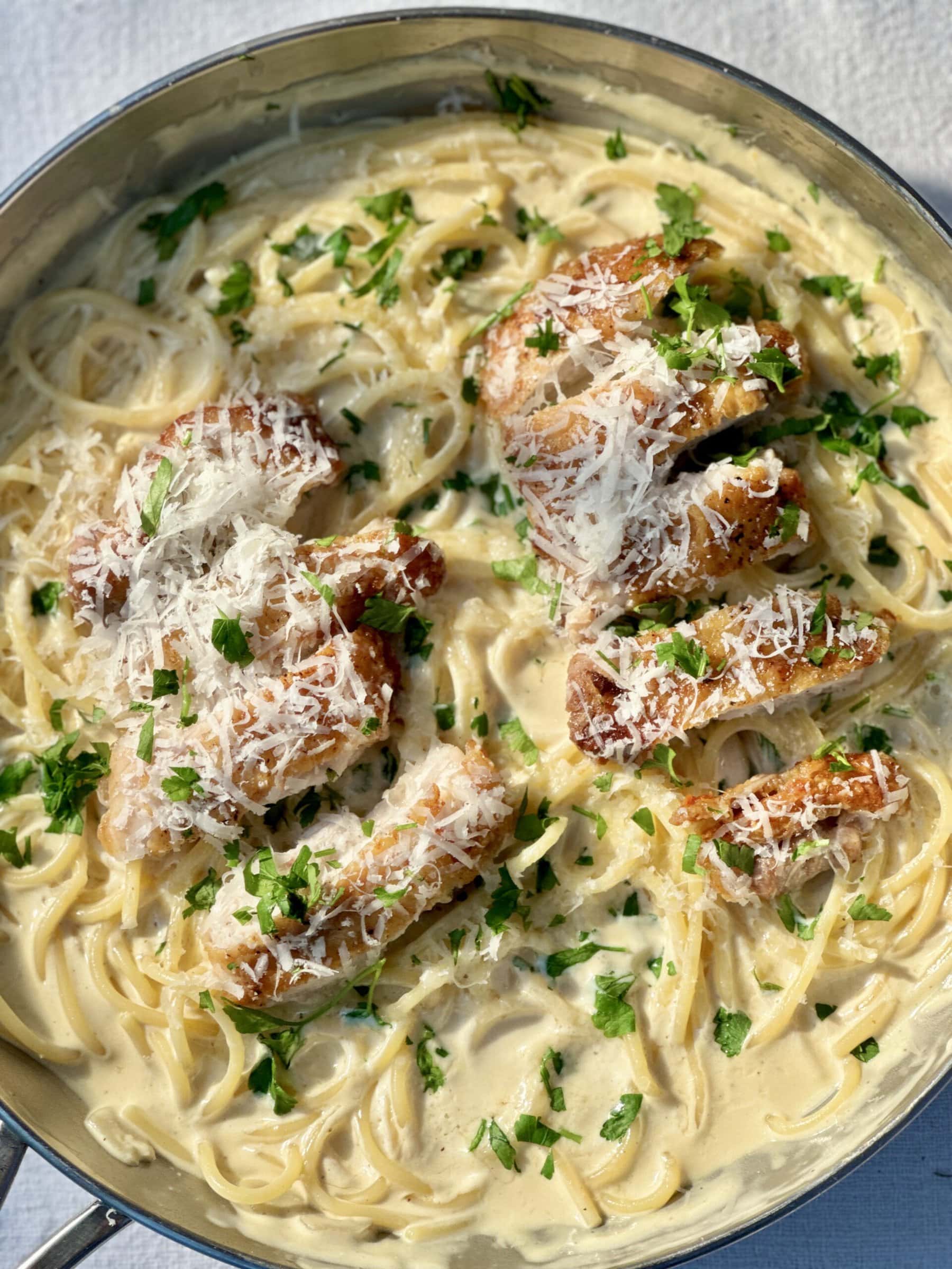 creamy chicken pasta in a pan with a fork, with chicken sliced on top..