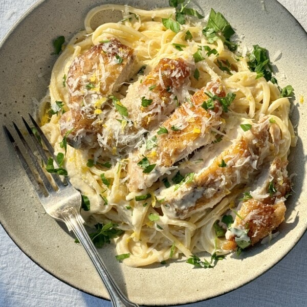 creamy chicken pasta in a bowl with a fork, with chicken sliced on top..