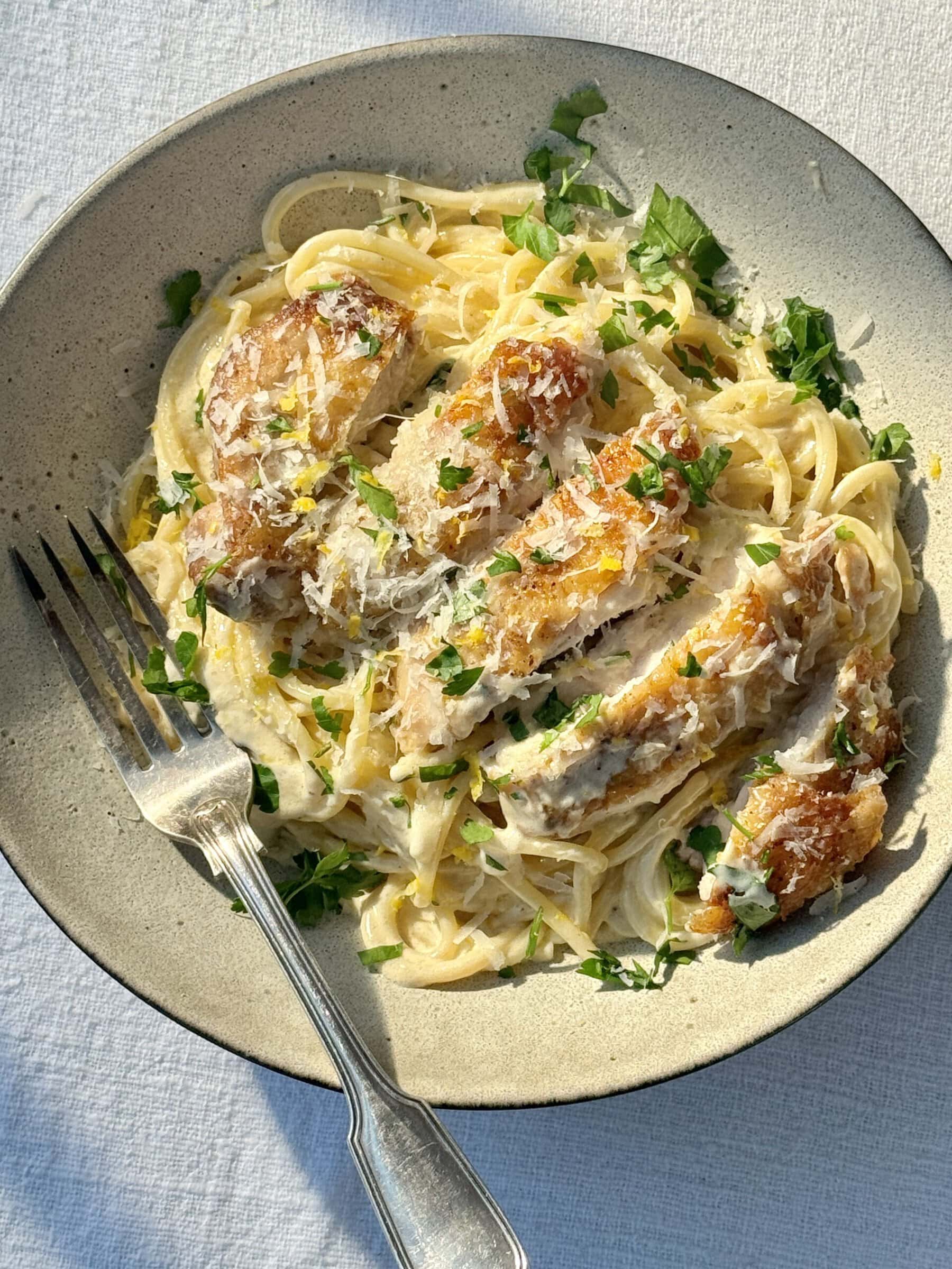 creamy chicken pasta in a bowl with a fork, with chicken sliced on top..