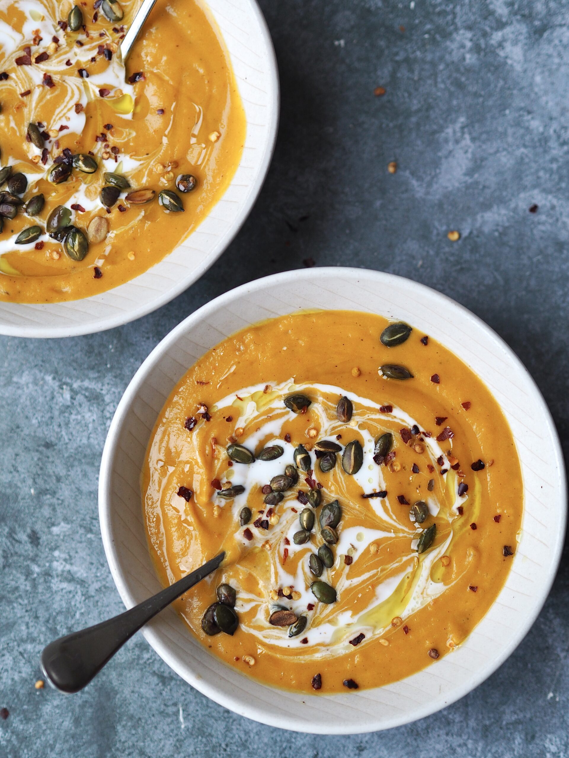 Close up of a bowl of butternut squash soup topped with coconut milk, seeds and dried chilli flakes.