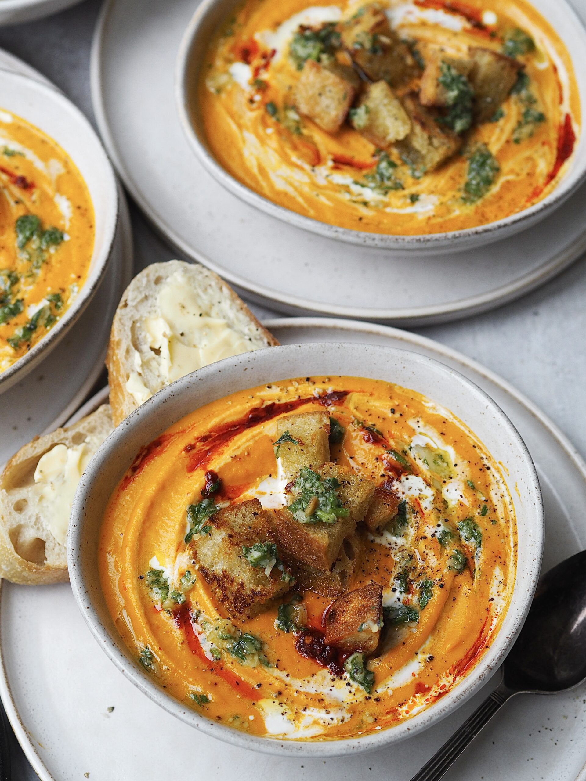 Close up of a bowl of roasted carrot soup topped with cream, harissa, croutons and pesto. 