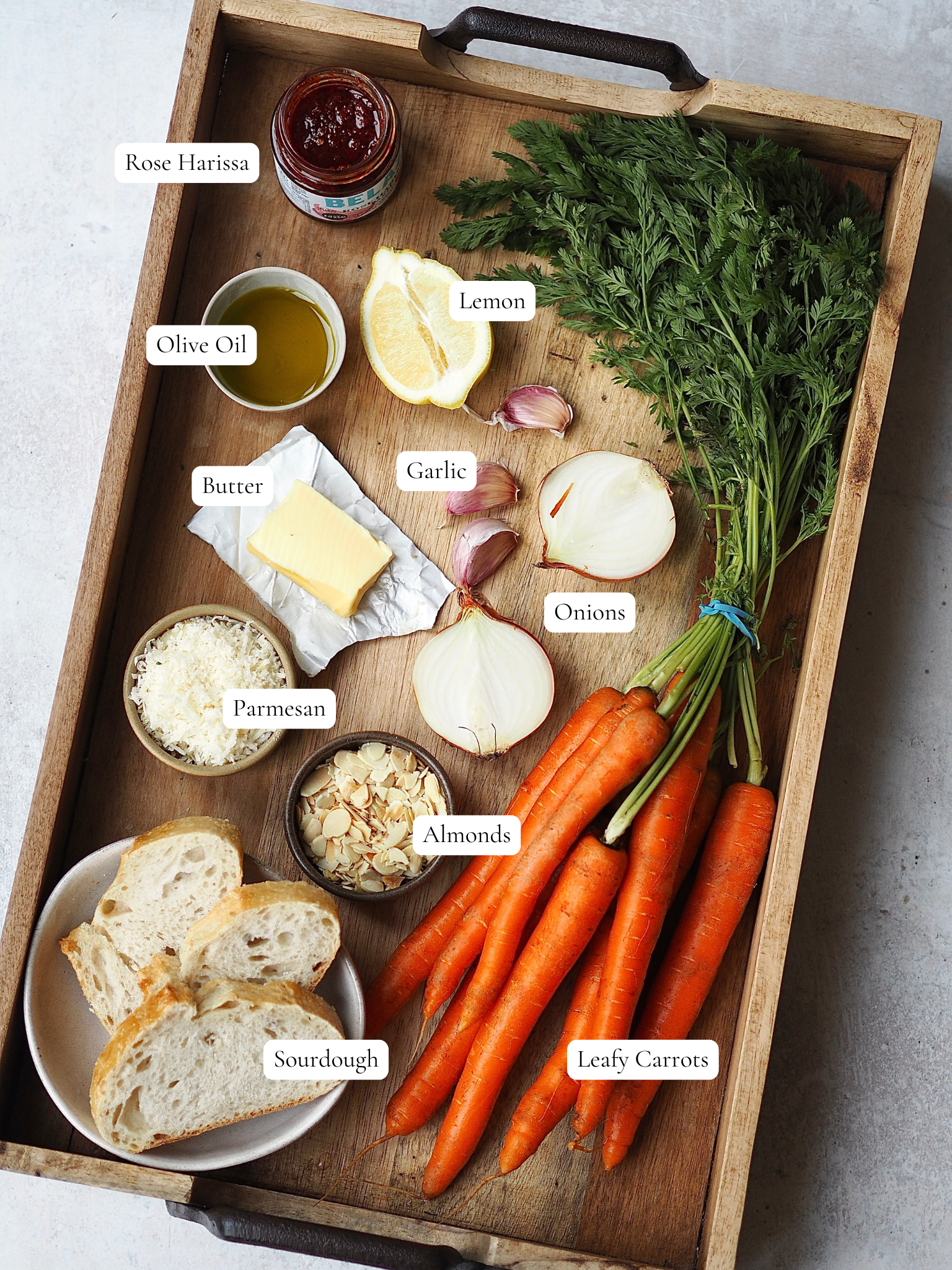 Labelled ingredients to make carrot and harissa soup on a wooden tray.