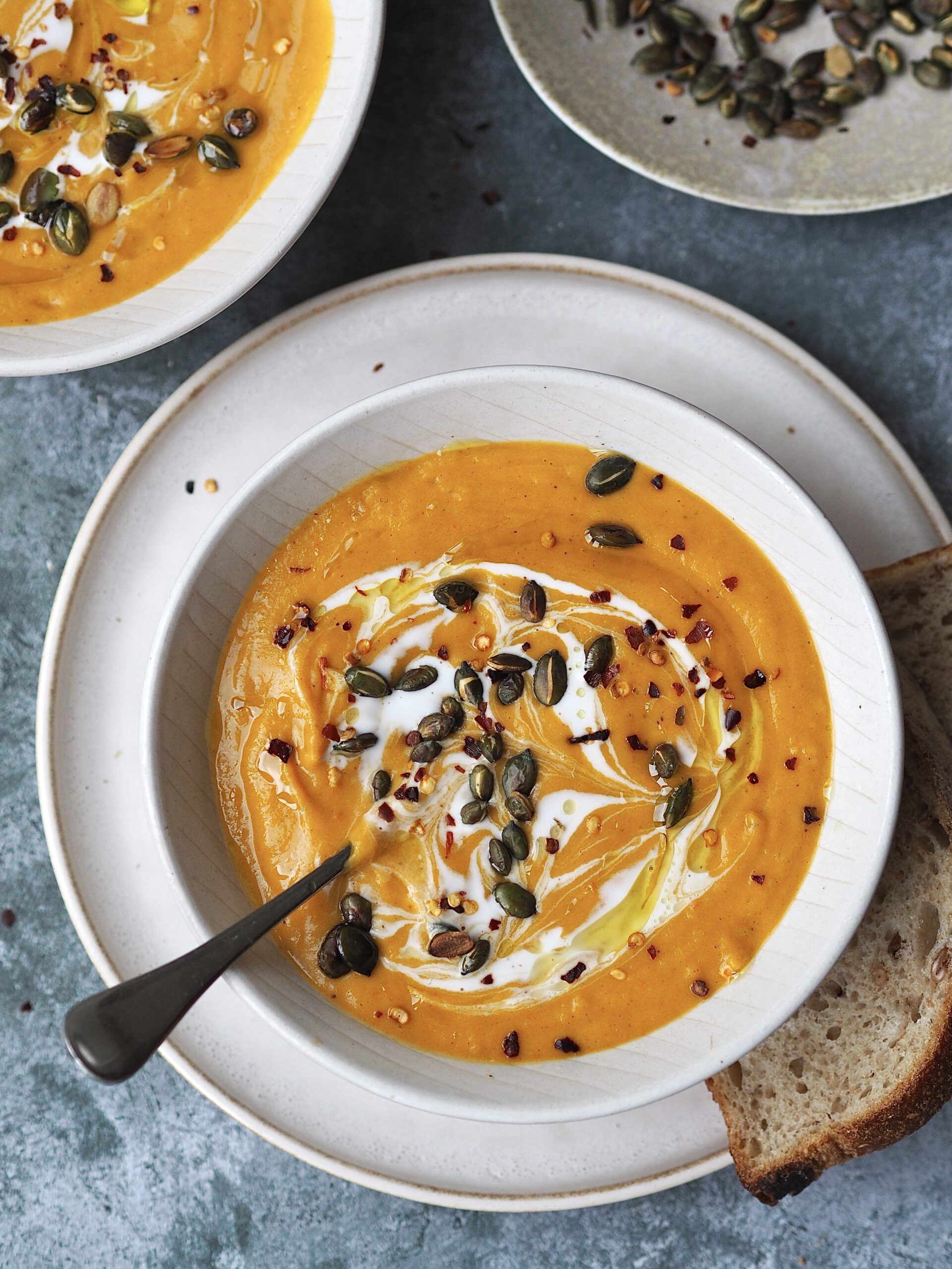 Squash soup in a white bowl on a white plate with a piece of bread on the side.