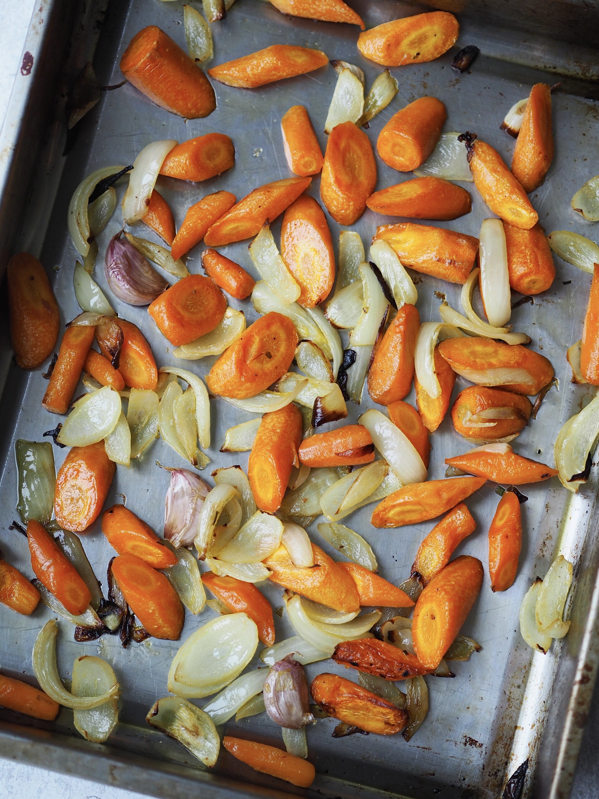 Roasted carrots, onions and garlic cloves on a roasting tray.