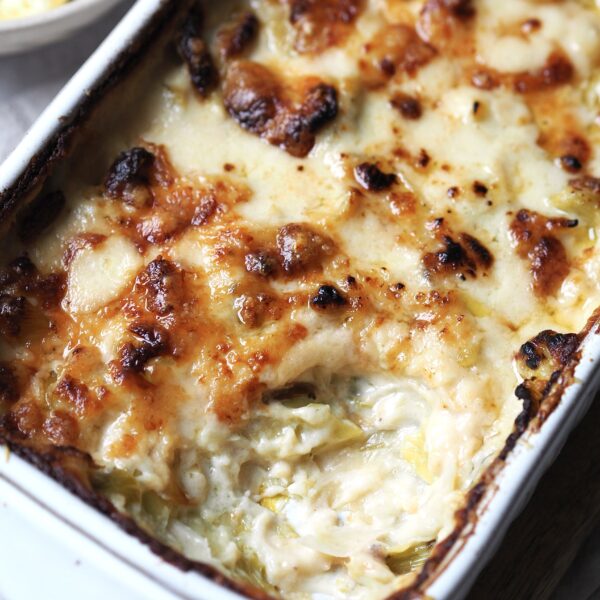 Close up of a dish of cheesy baked leeks with a spoonful missing.