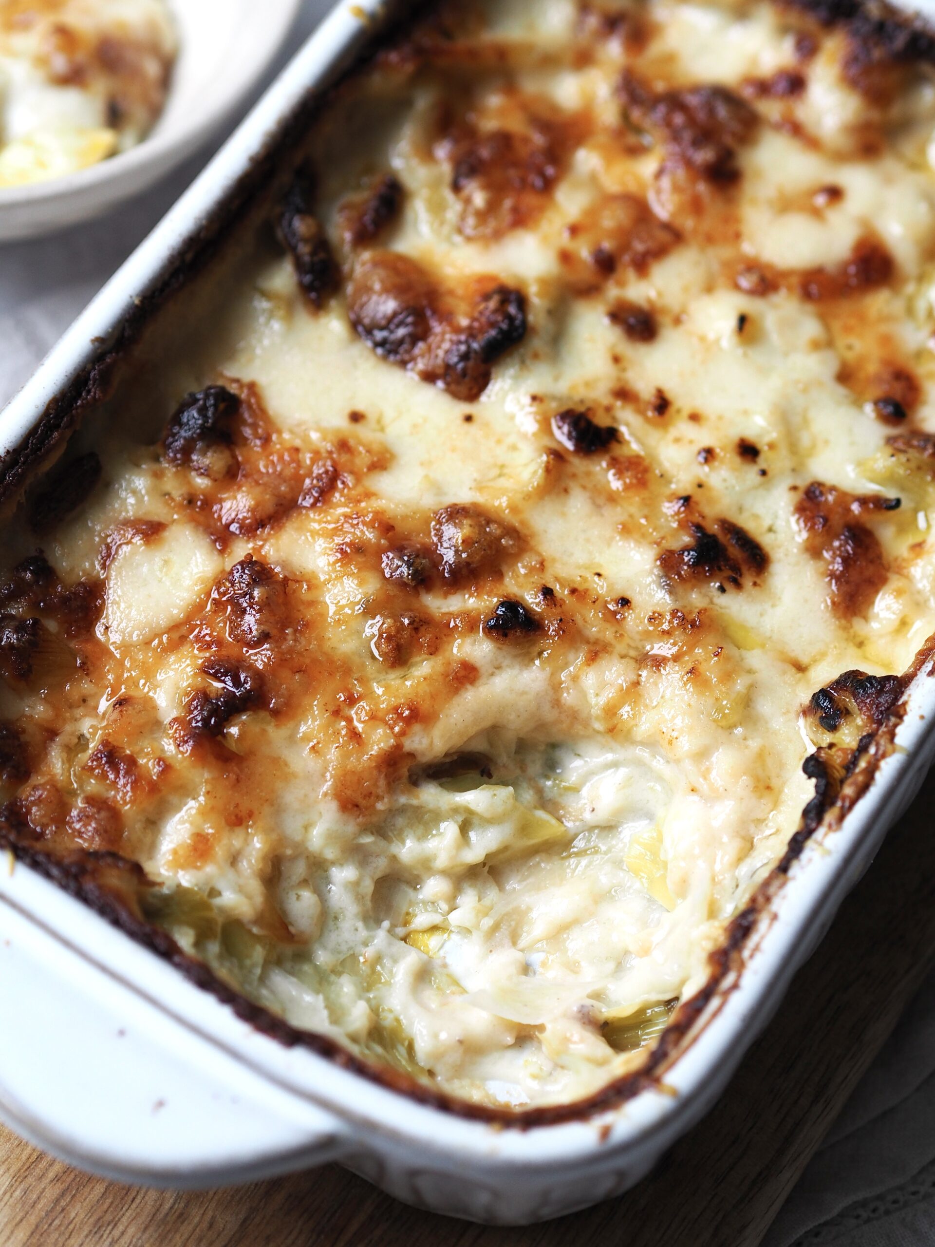 Close up of a dish of cheesy baked leeks with a spoonful missing. 