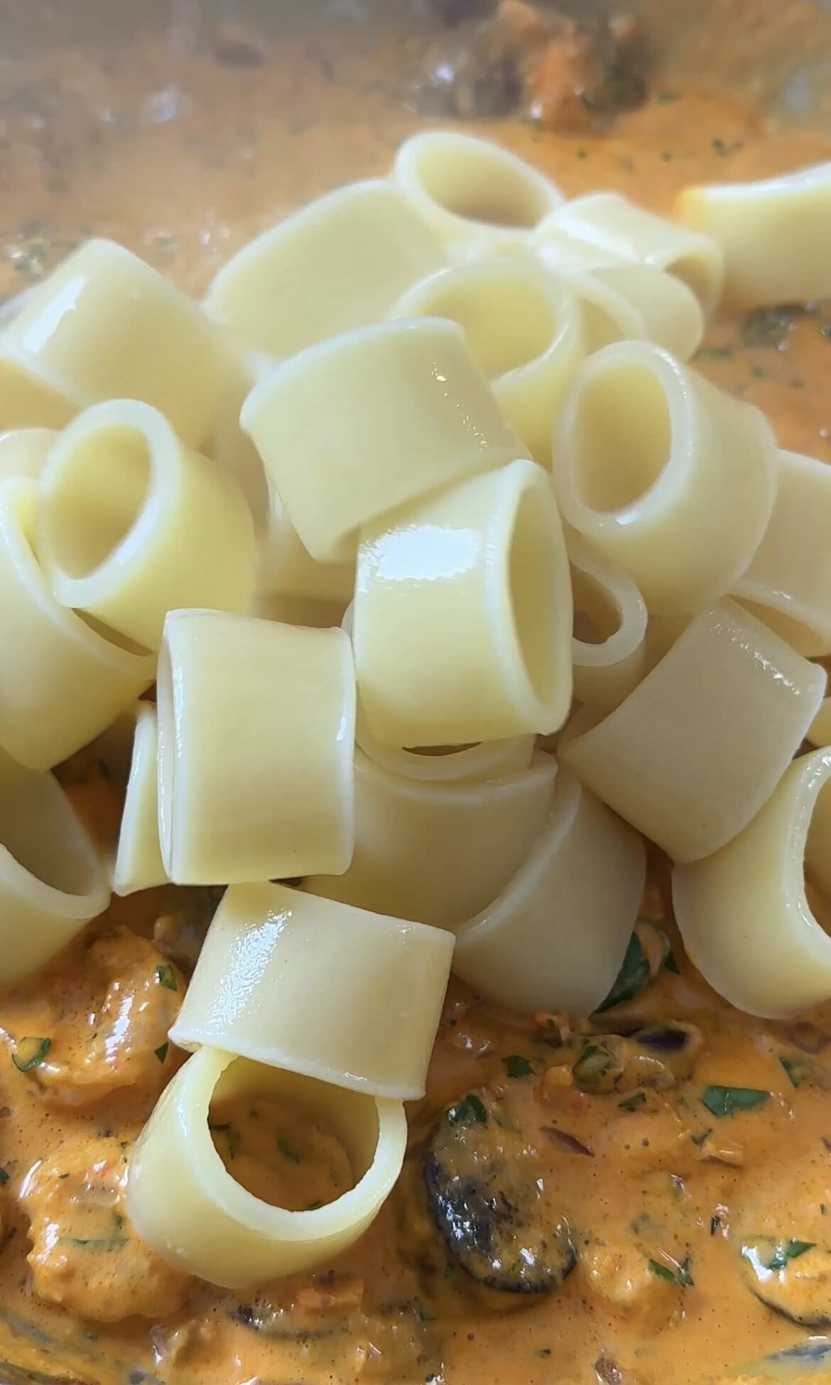 adding pasta to the prawn and chorizo sauce.