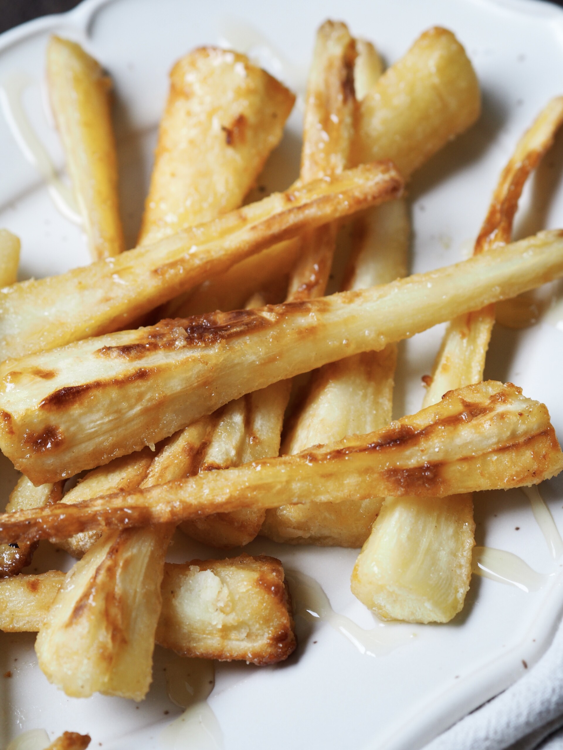 Close up of honey glazed roasted parsnips on a white serving platter.