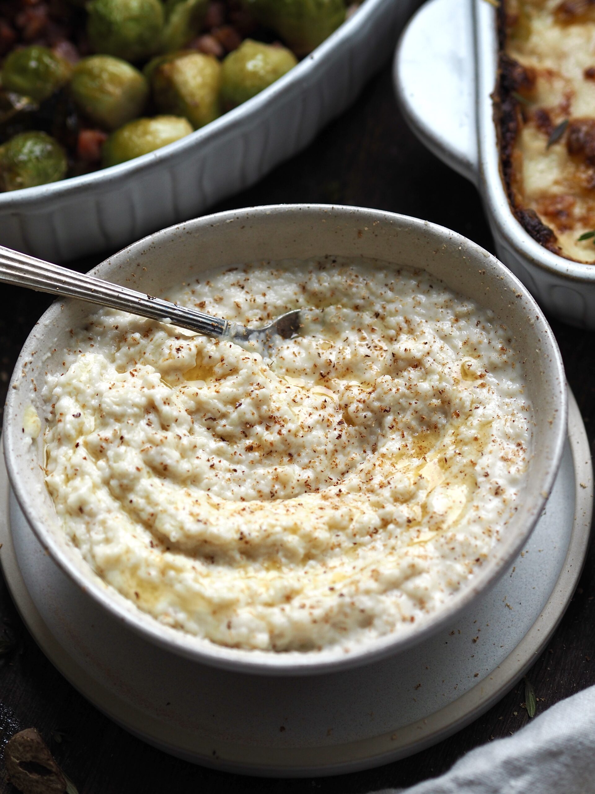 Bowl of bread sauce with dishes of bacon sprouts and cheesy leeks in the background.