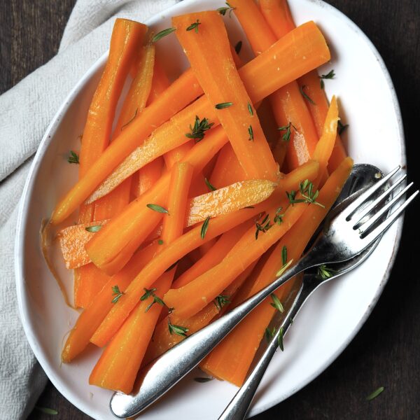 White serving dish of glazed carrots with fresh thyme sprinkled over the top.