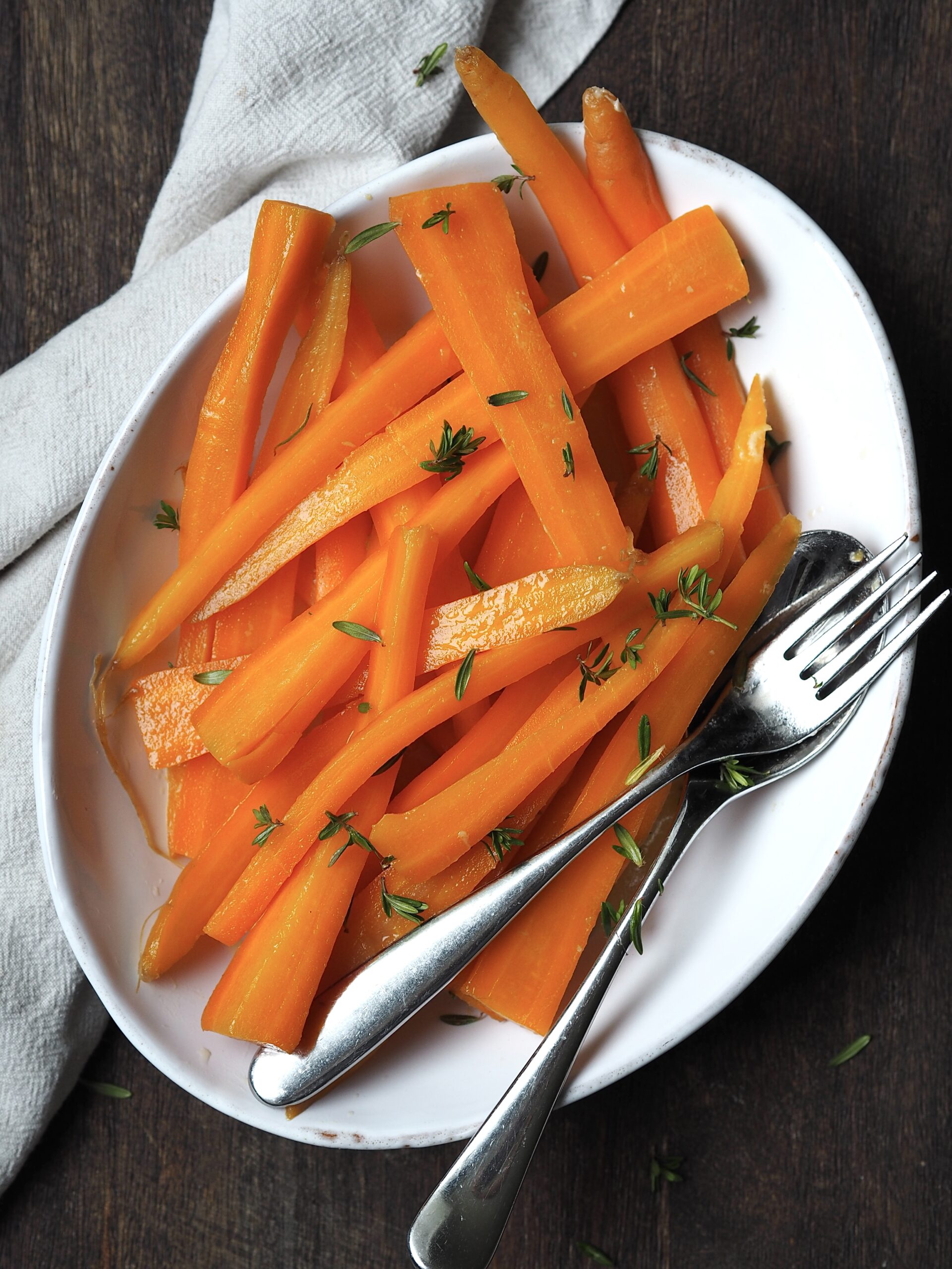 White serving dish of glazed carrots with fresh thyme sprinkled over the top.