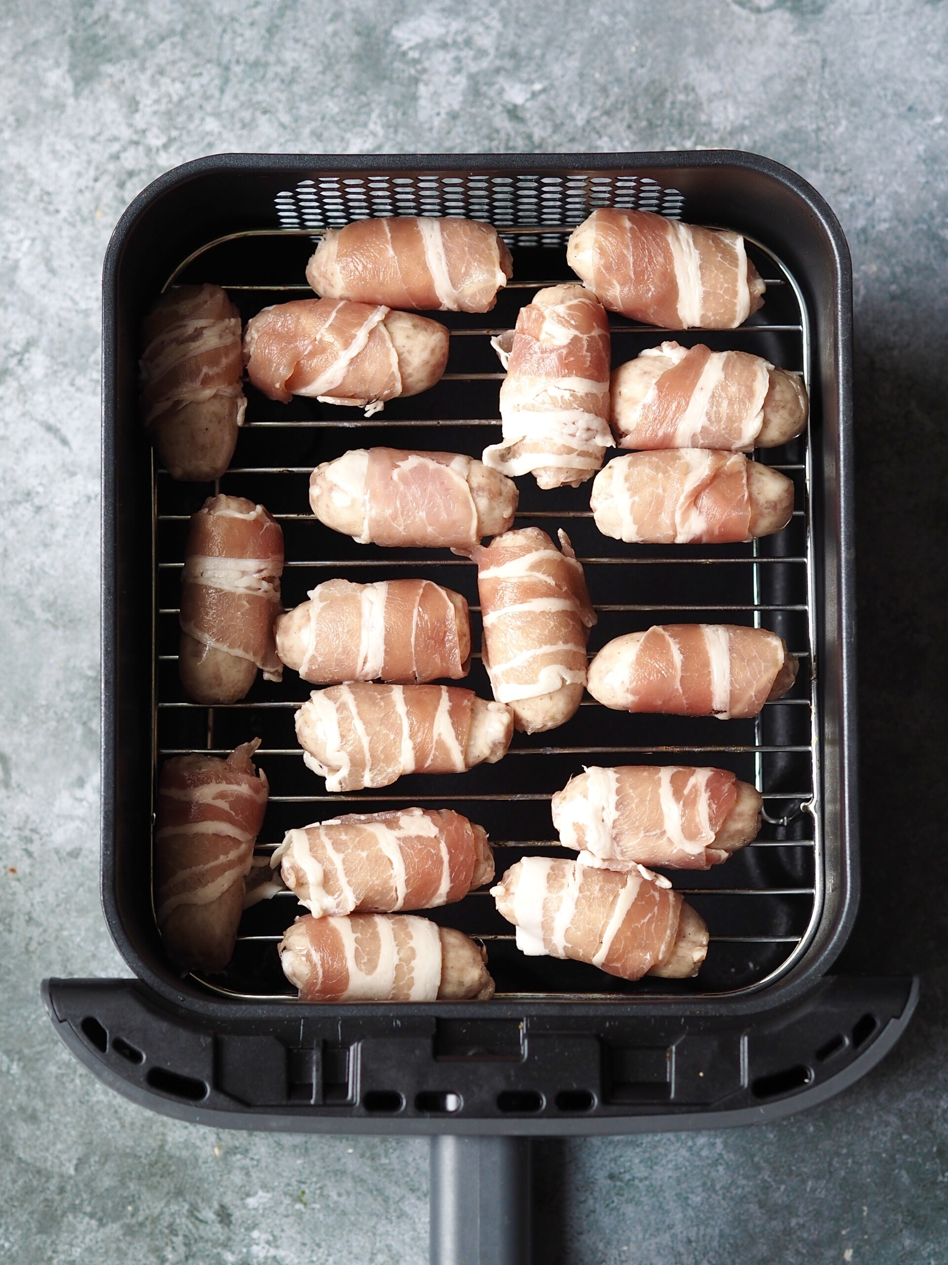 Uncooked pigs in blankets in an air fryer basket.