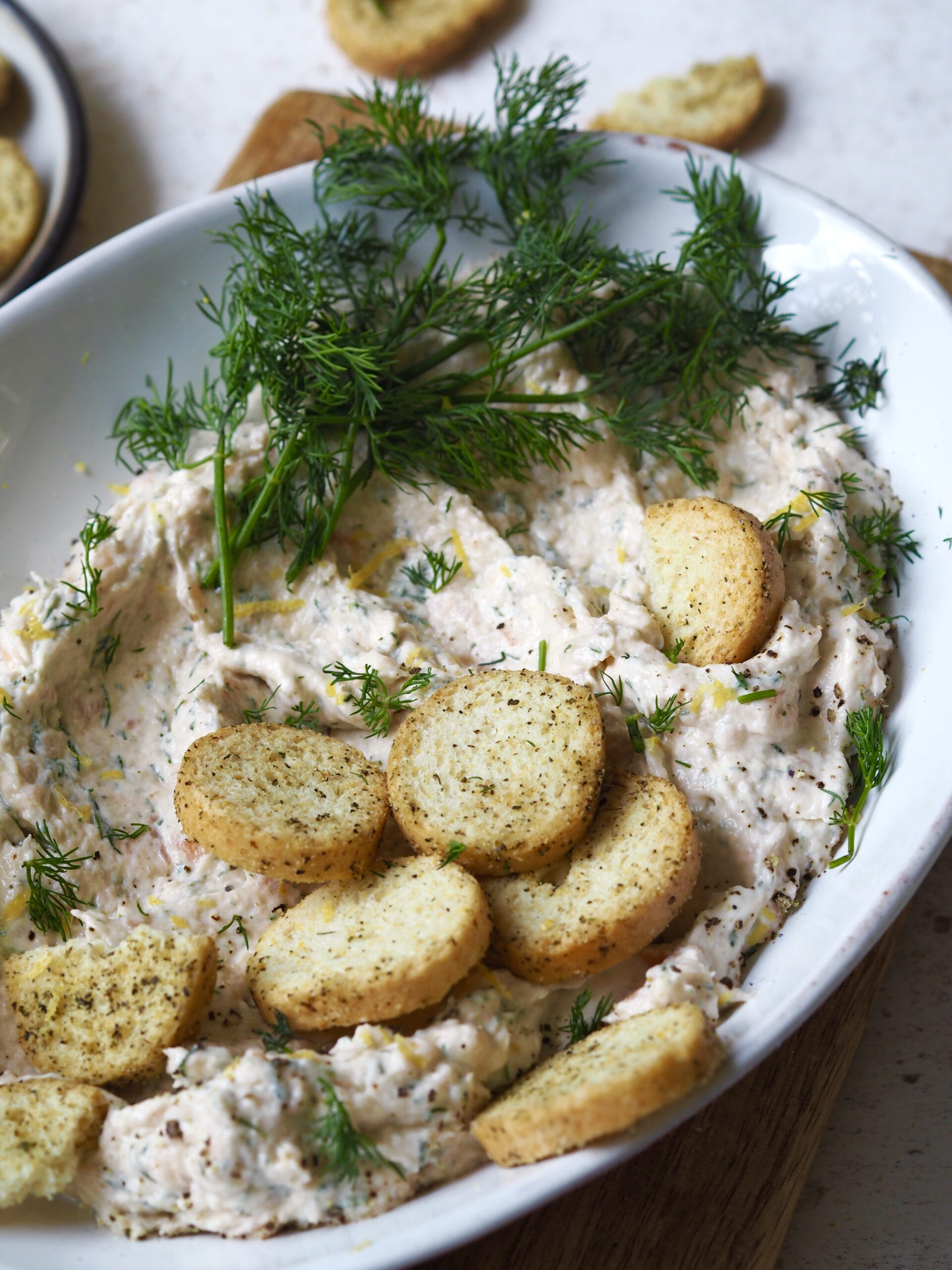 Bowl of salmon pate topped with fresh dill and crostini.