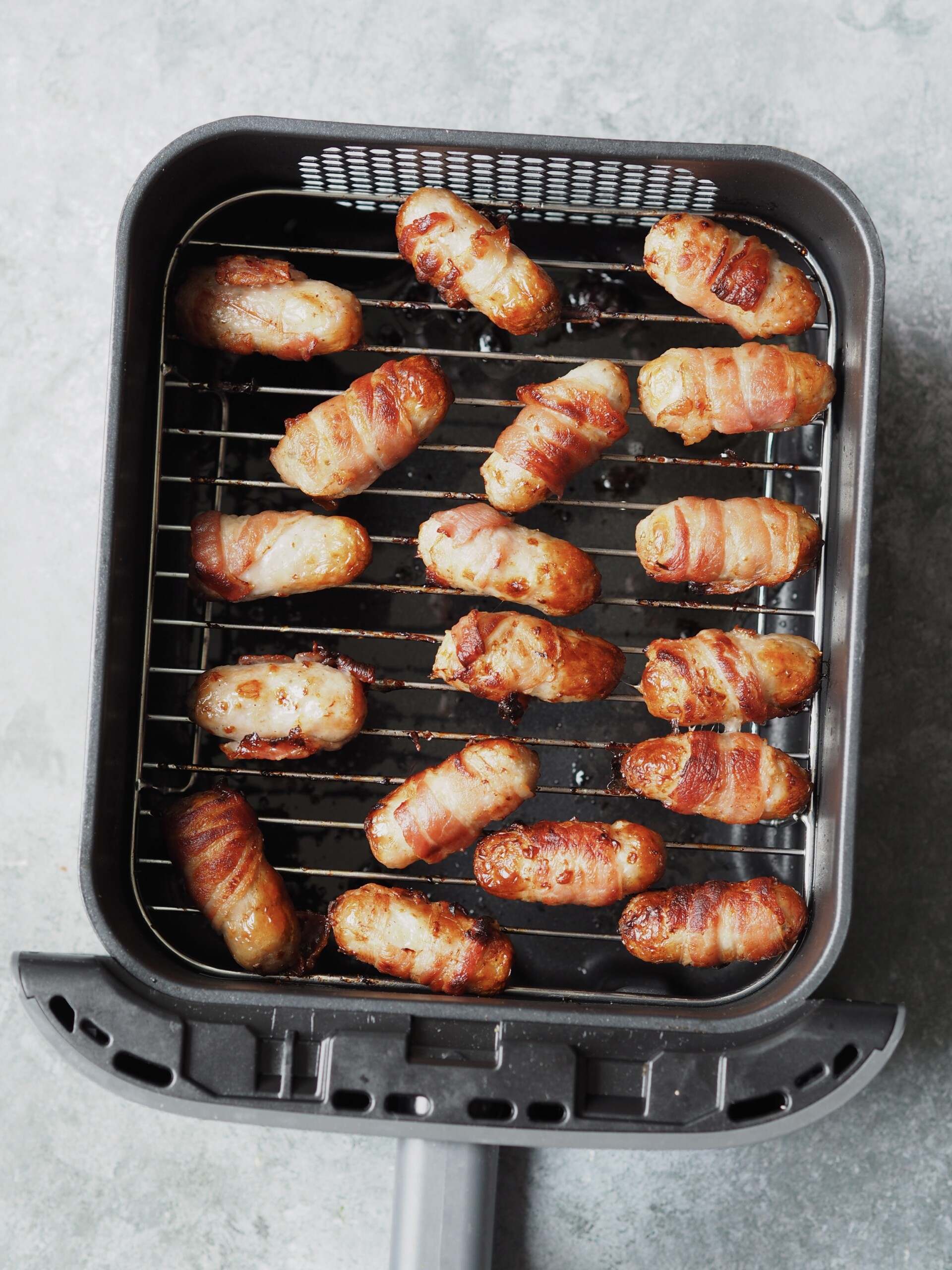 Cooked pigs in blankets in an air fryer basket.