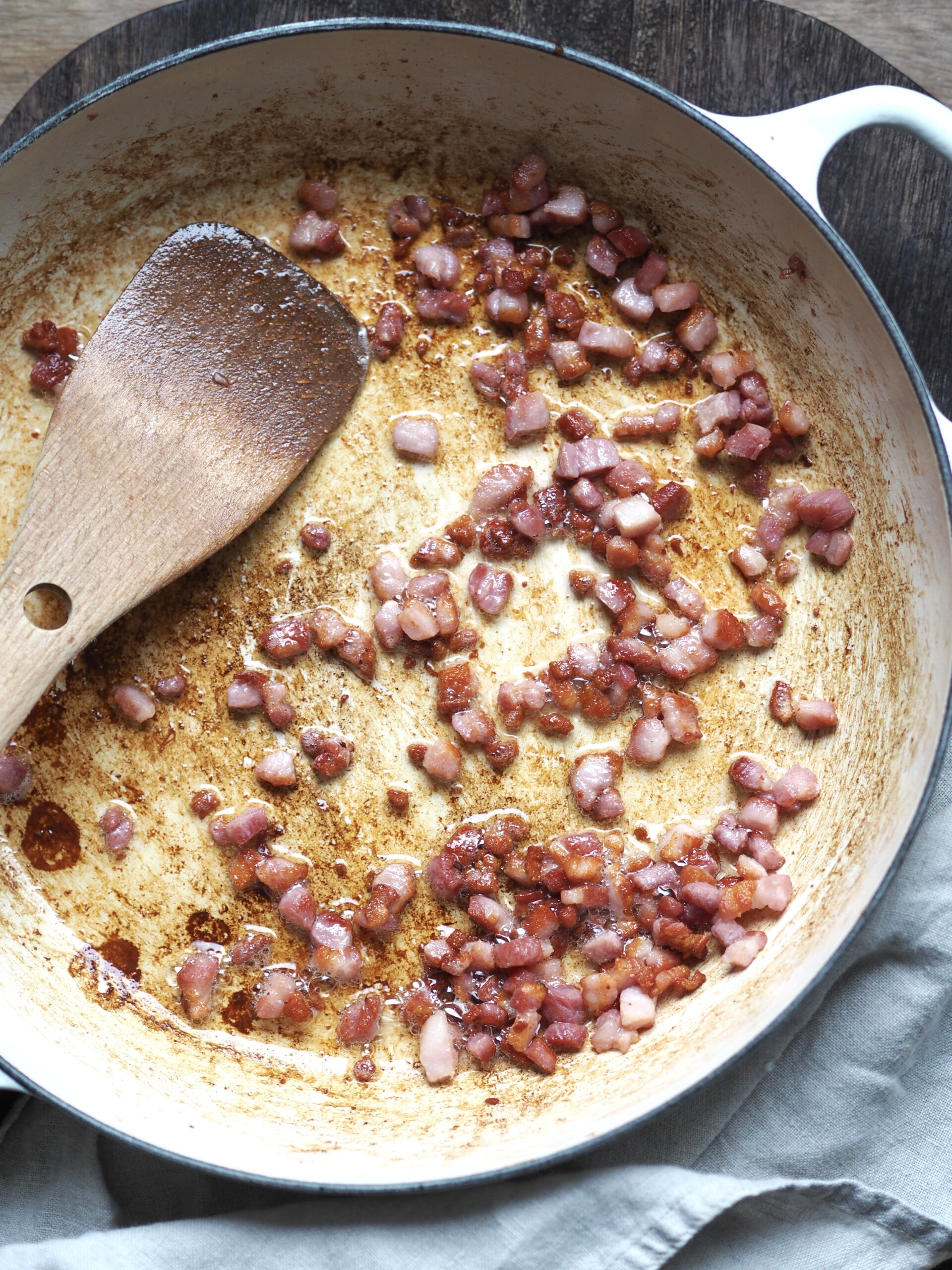 Bacon lardons frying in a white shallow casserole dish.