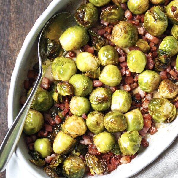 White oval serving dish of brussels sprouts with bacon pieces.